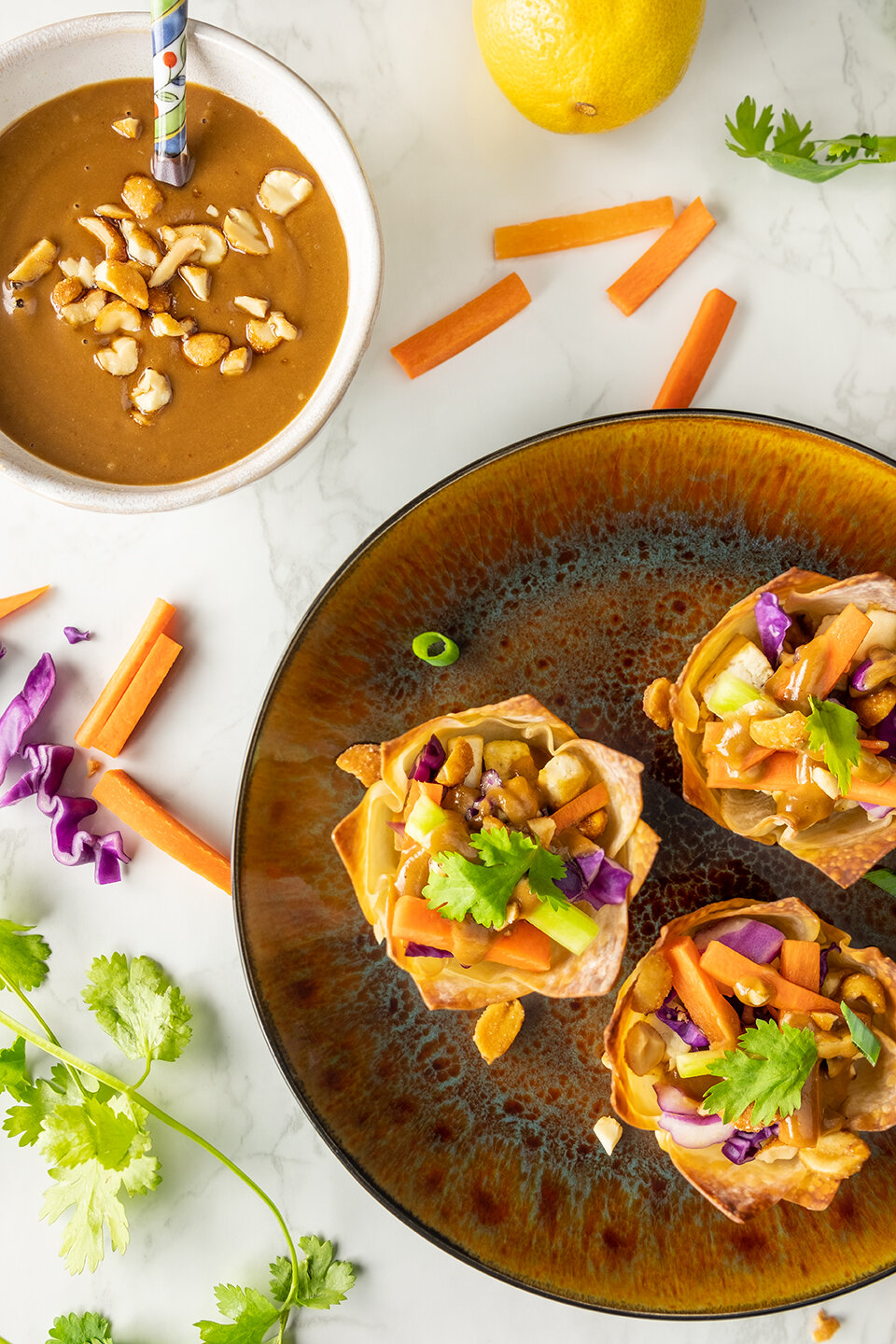  Three Thai tofu wonton cups on a small appetizer plate.  One small bowl with peanut sauce on the side with a spoon. 