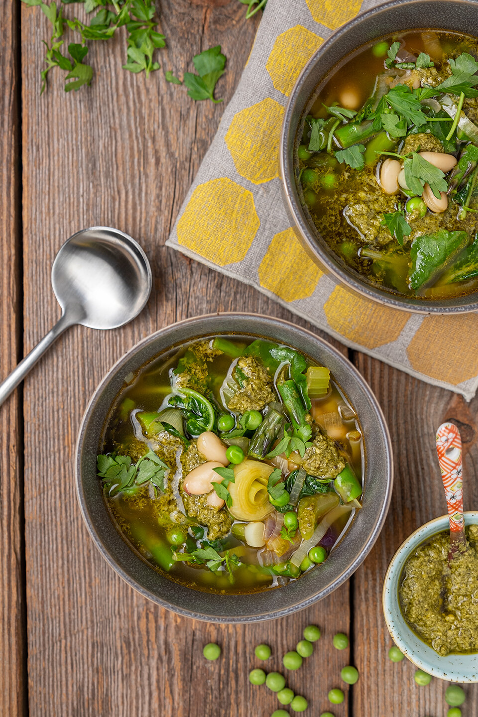  Two bowls of Spring Soup with white beans. Peas, parsley and pesto in on a rustic wood background. 