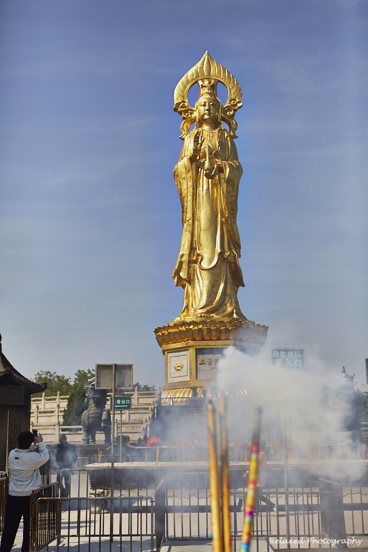 This image shows the 70 meter tall Bhudda statue that so many people come to worship. In the foreground there are some some incense sticks burning.