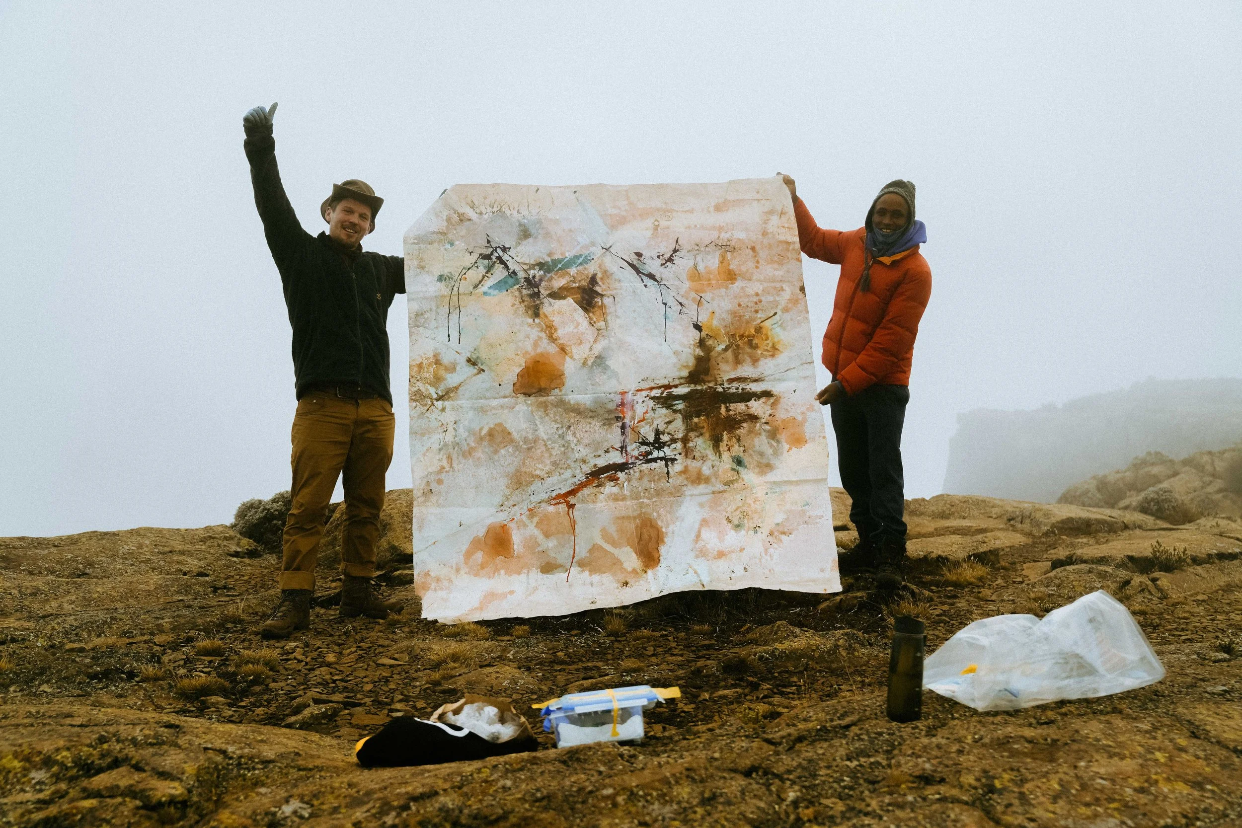 Artist Peter Kettle and his guide holding a large painting made during the ascent of Mount Kenya.