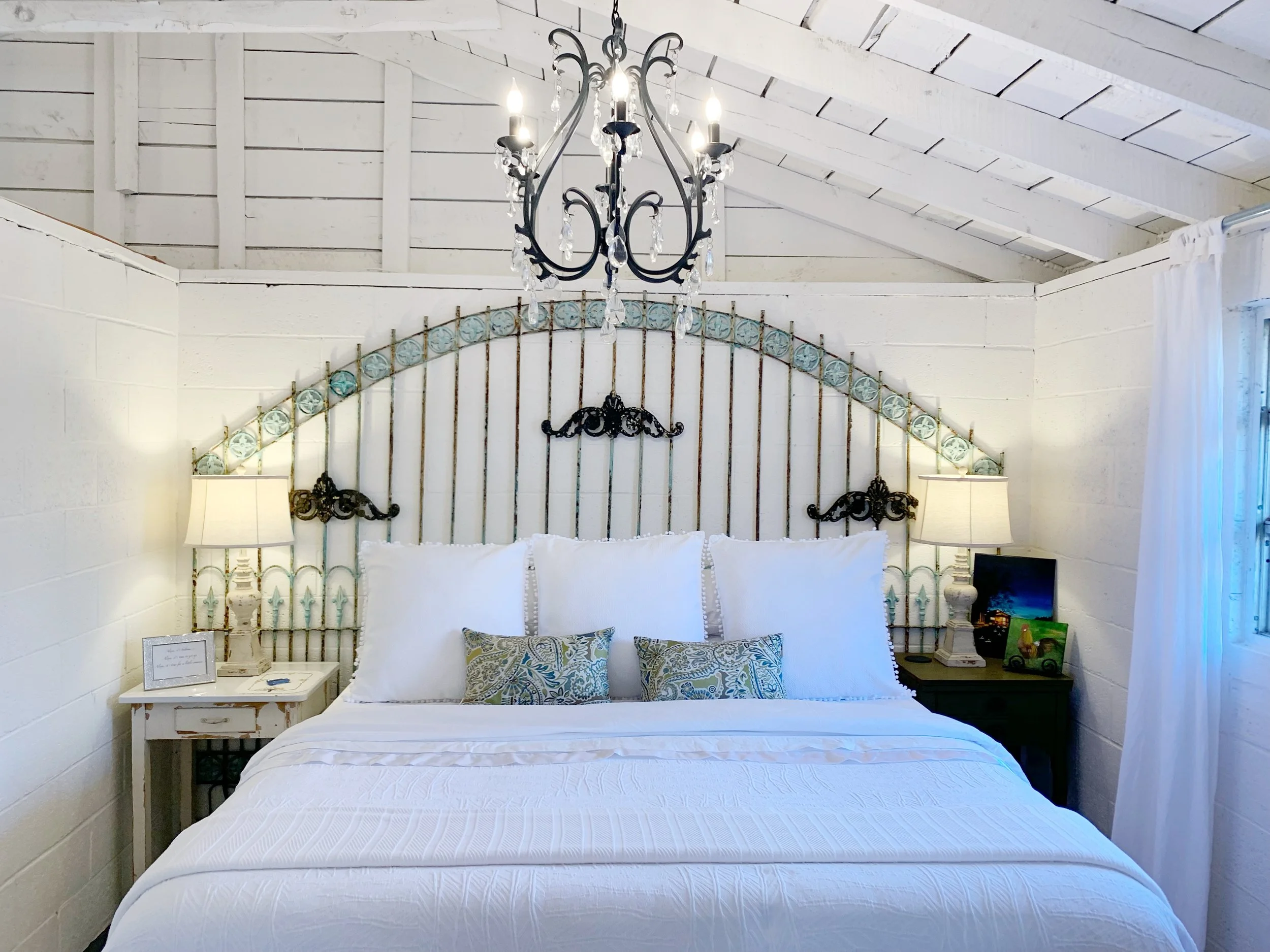 IRON GATES FROM CULPEPPER’S OTTO SALVAGE and mounted to the wall with pipe fittings.. BEDSIDE TABLES FROM THE QUEEN OF HEARTS . PAINTINGS BY LOCAL ARTIST, MACK ANDERSON
