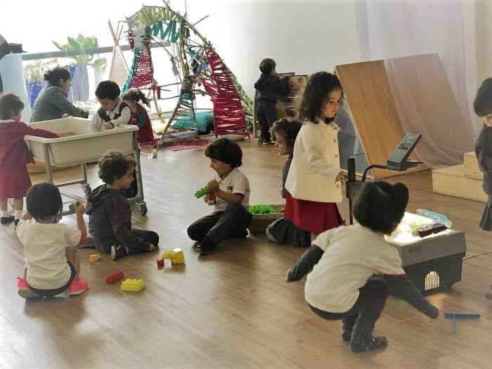 Alunos realizam investigações em uma ampla sala de aula e utilizam brinquedos e projetor.