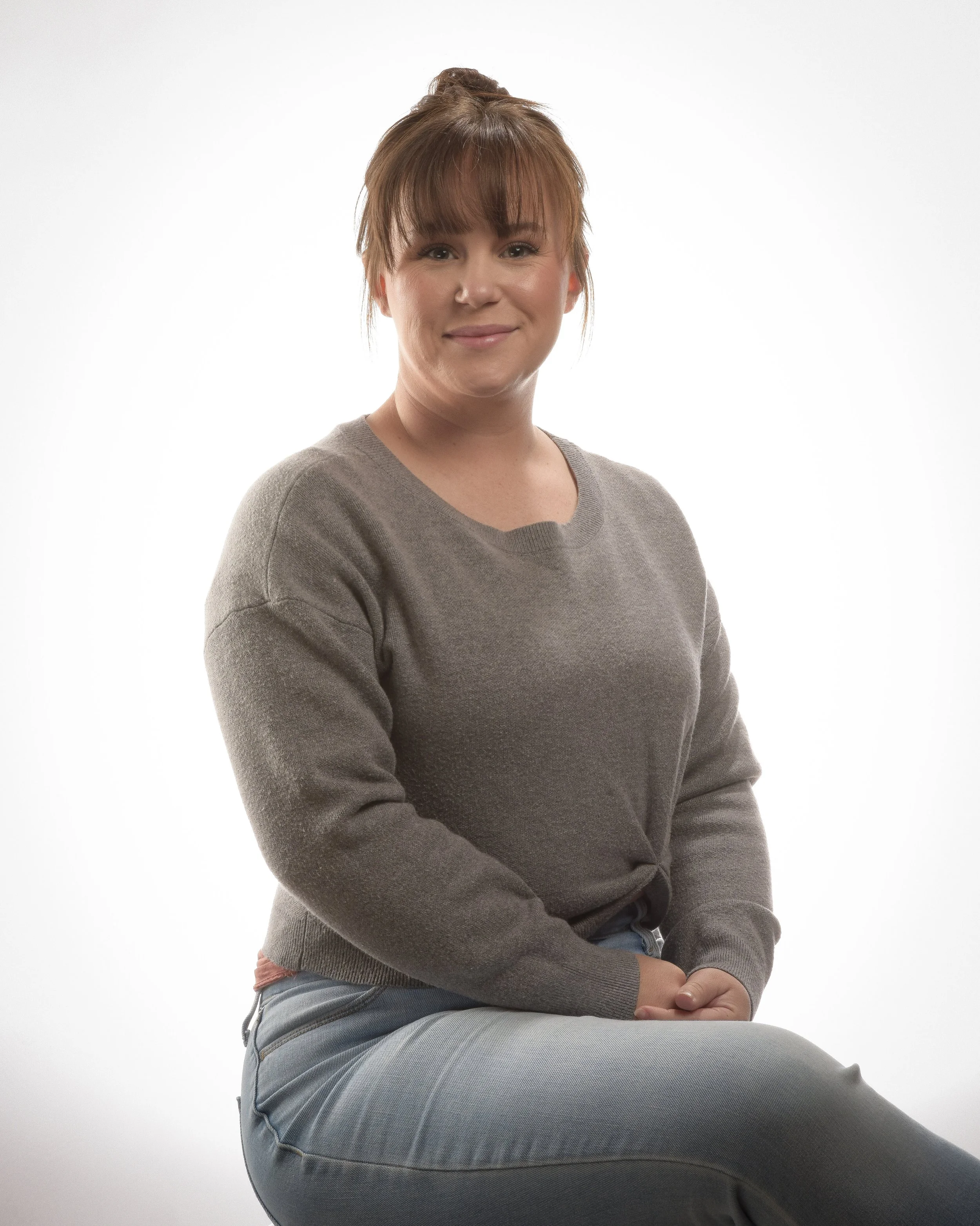 A young woman with her hair done in a bun. She is wearing a grey sweater.