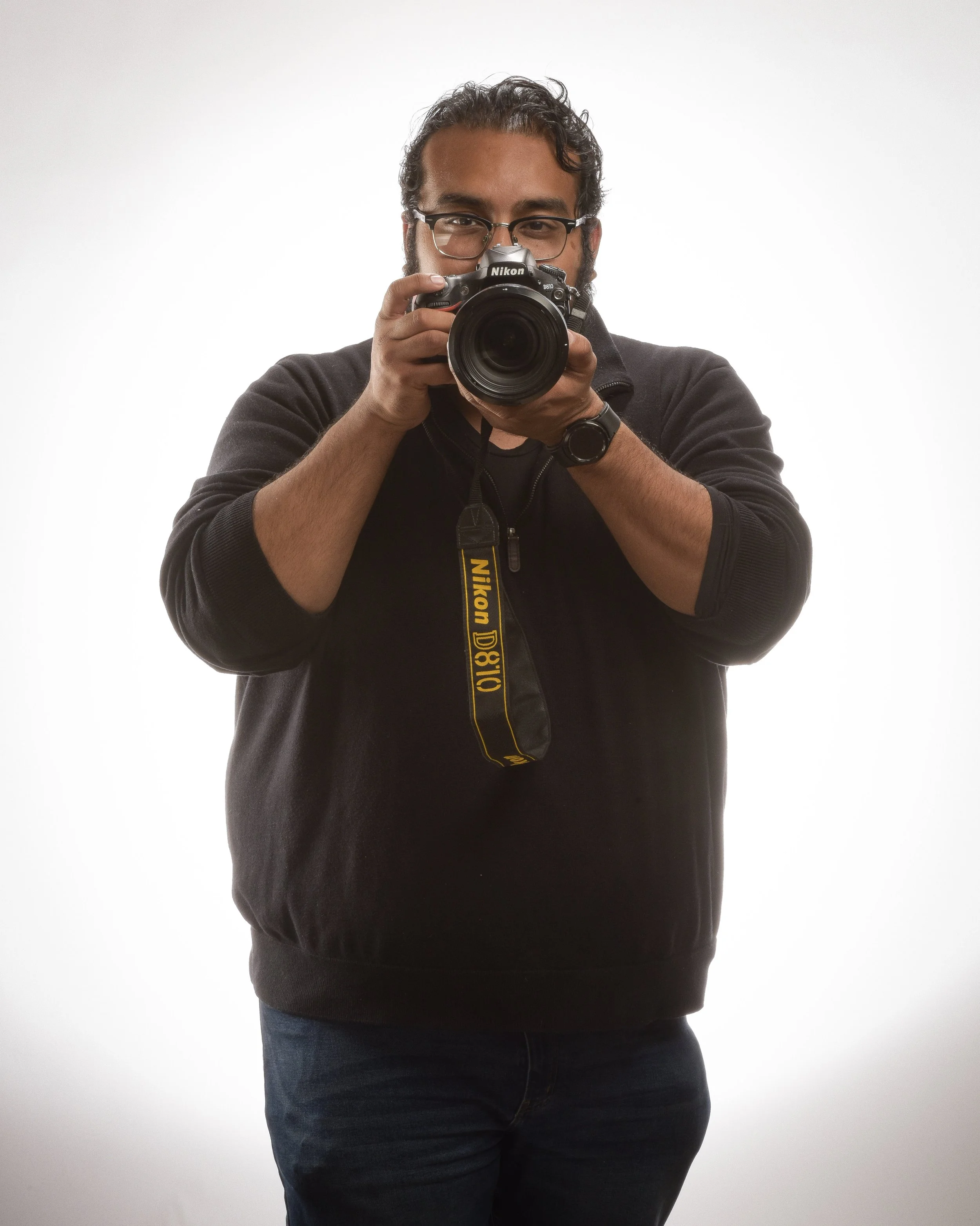 An image of a young man posed with a camera as if ready to take your photo.