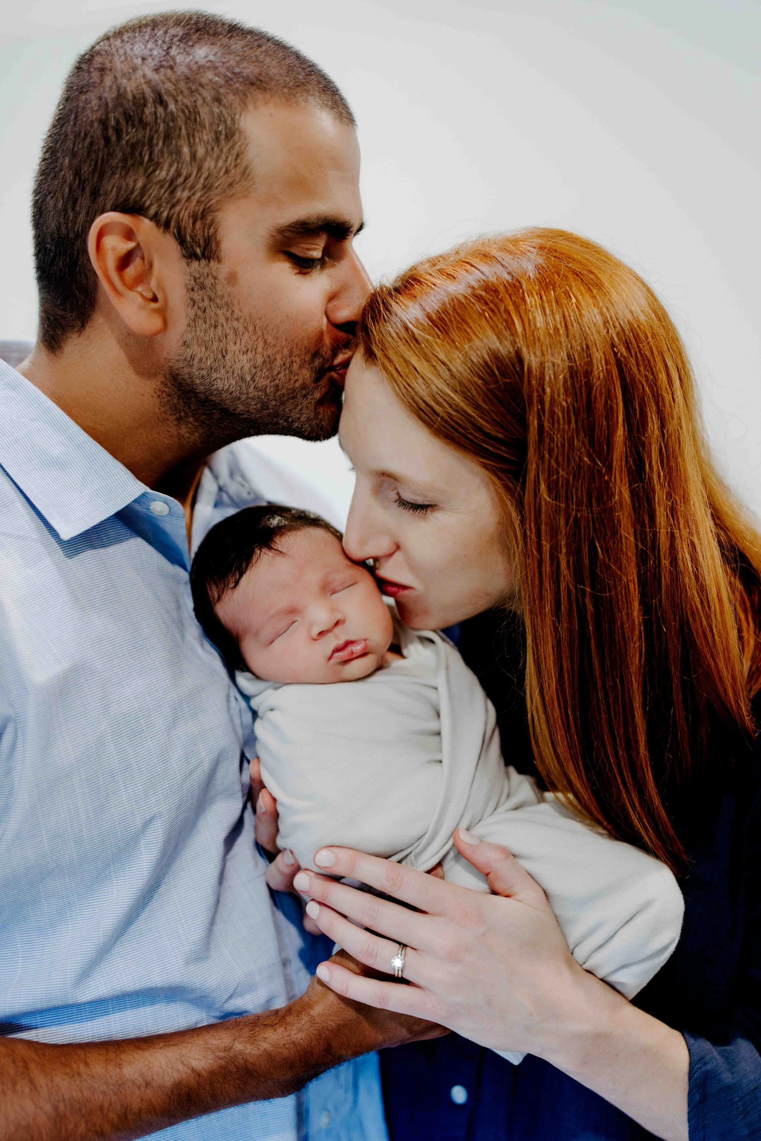 Mom and dad kissing newborn’s head in natural light newborn photography at home