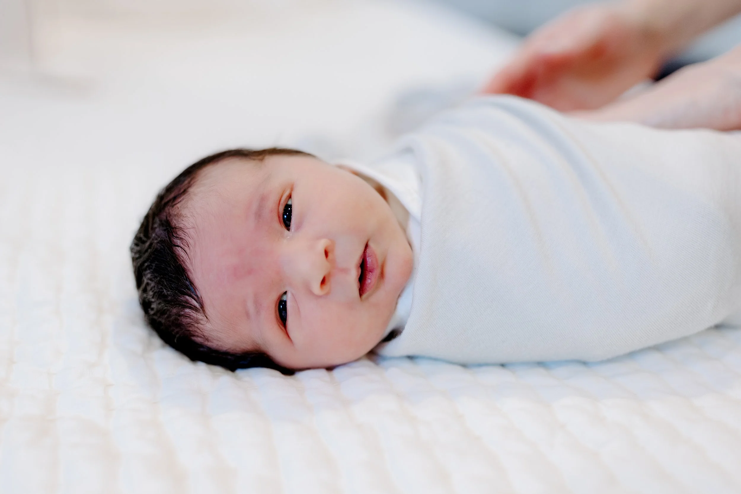 close-up of newborn face swaddled in blannket with his eyes open