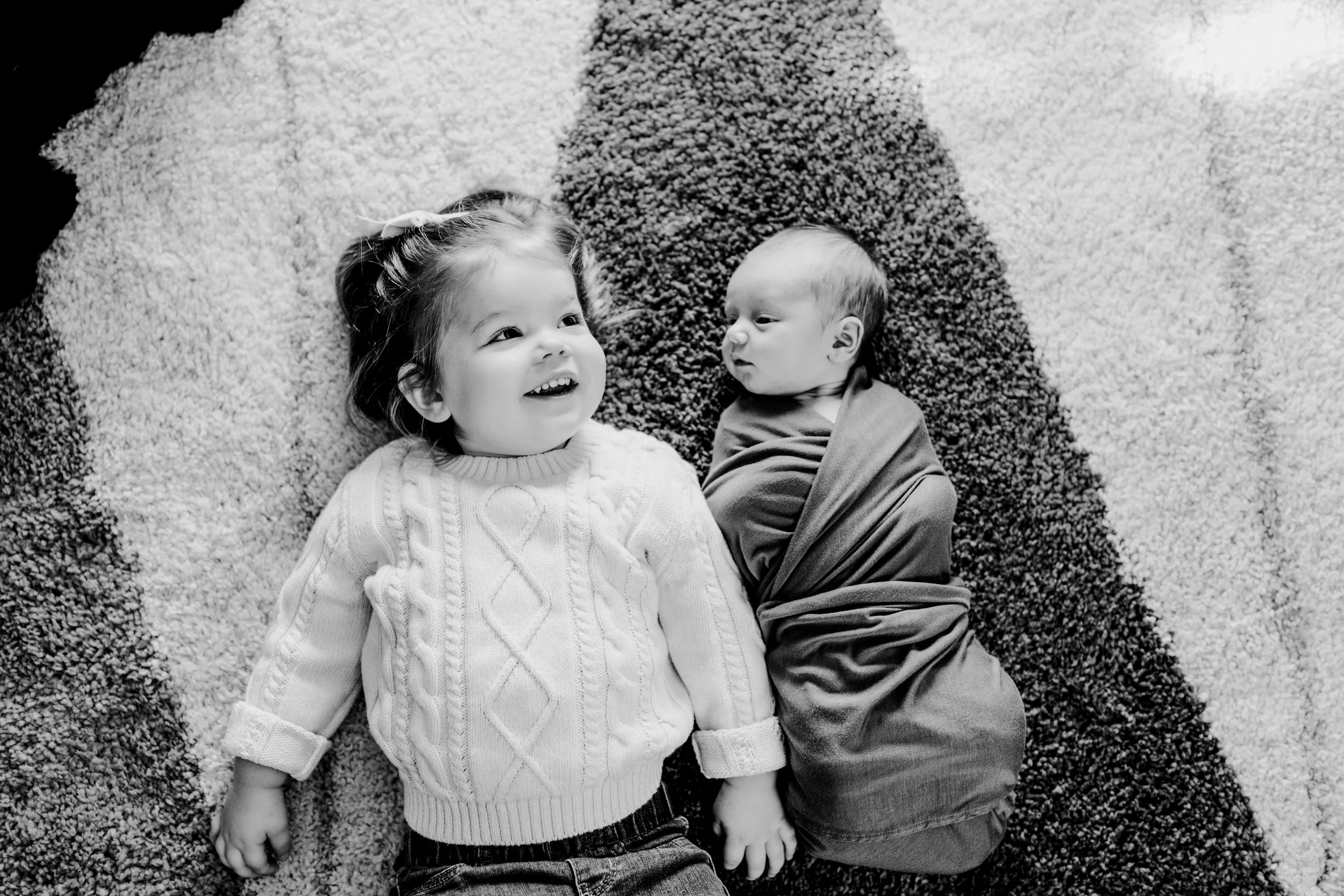 Toddler sister laying next to newborn during in home newborn photography session