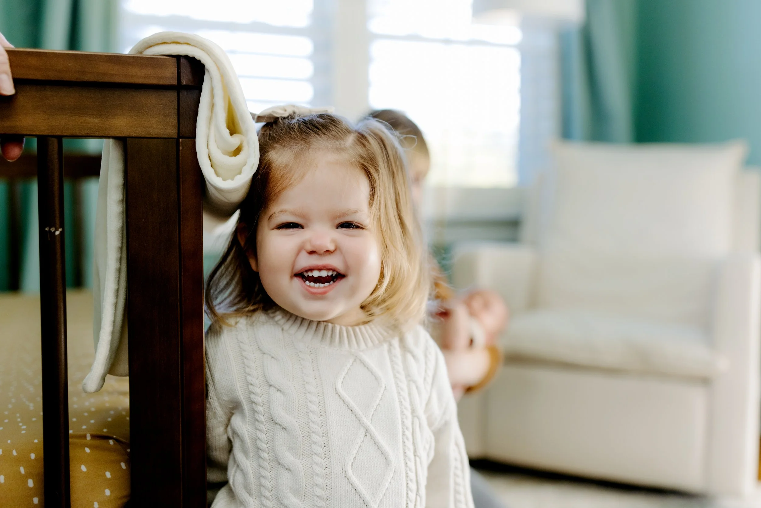 toddler big sister laughing standing by baby’s crib during newborn session