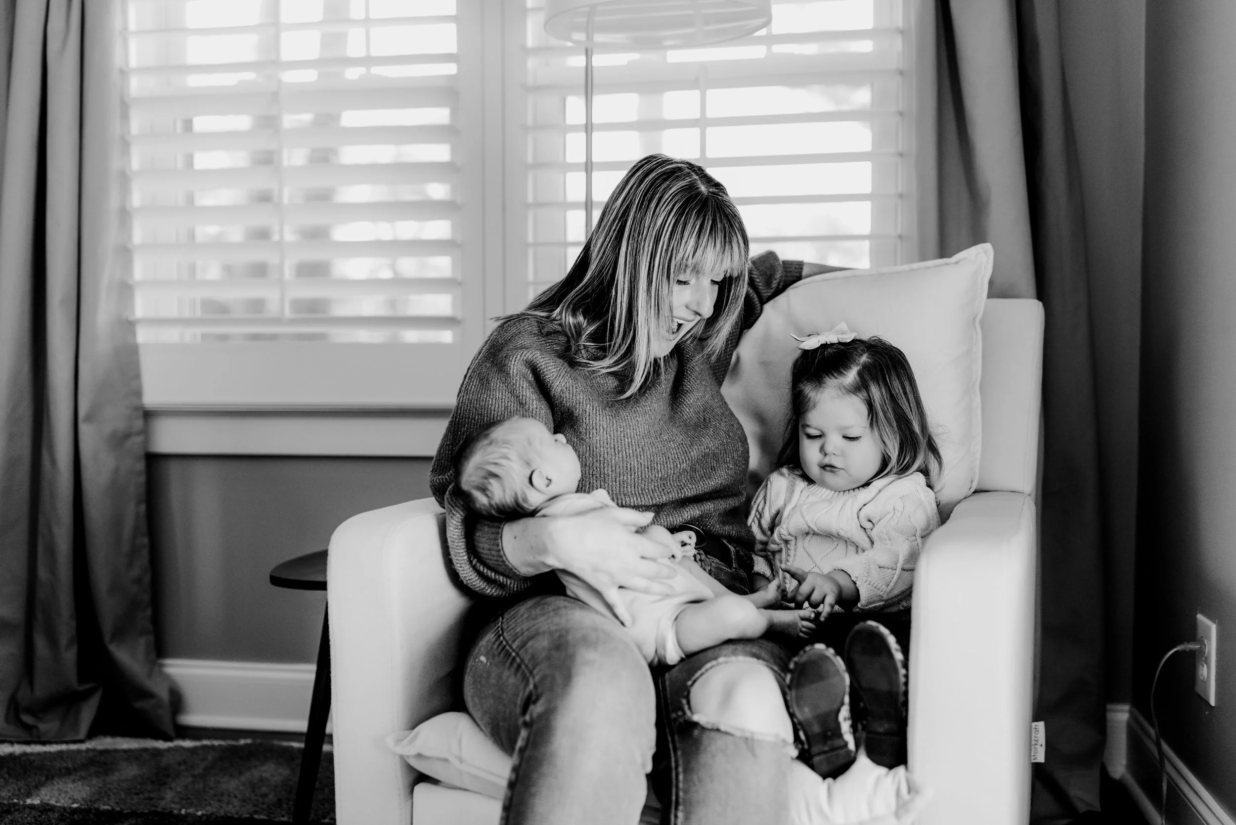 mom, toddler and newborn snuggling on a rocking chair in baby’s nursery during a newborn photo session