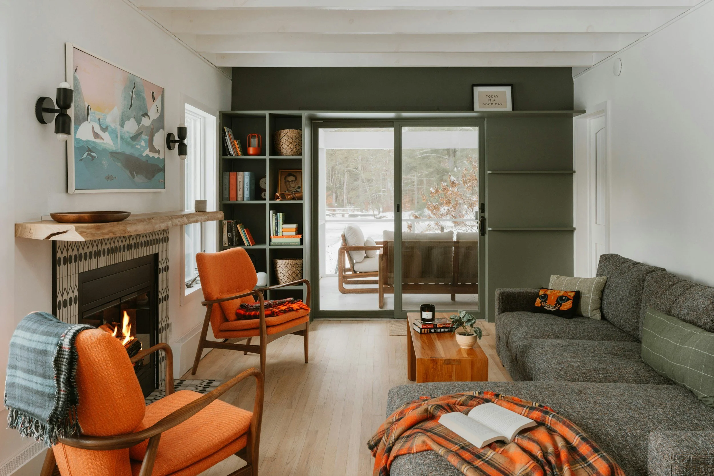 Cozy, organized living room with orange chairs by a fireplace, gray sofa, built-in shelves, and sliding glass doors leading to an outdoor seating area.