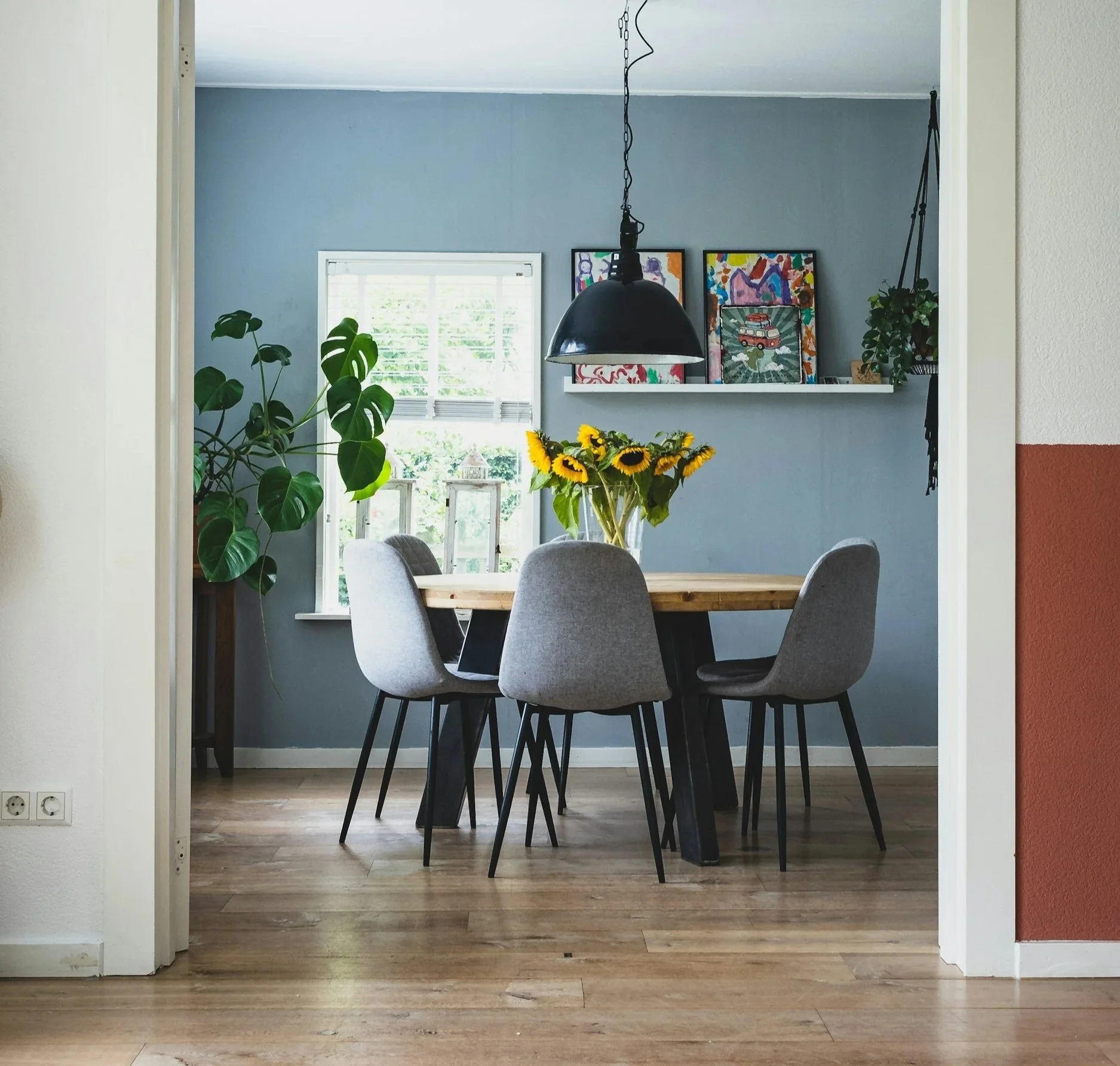 Dining room with round table, chairs, sunflowers, surrounded by plants and artwork