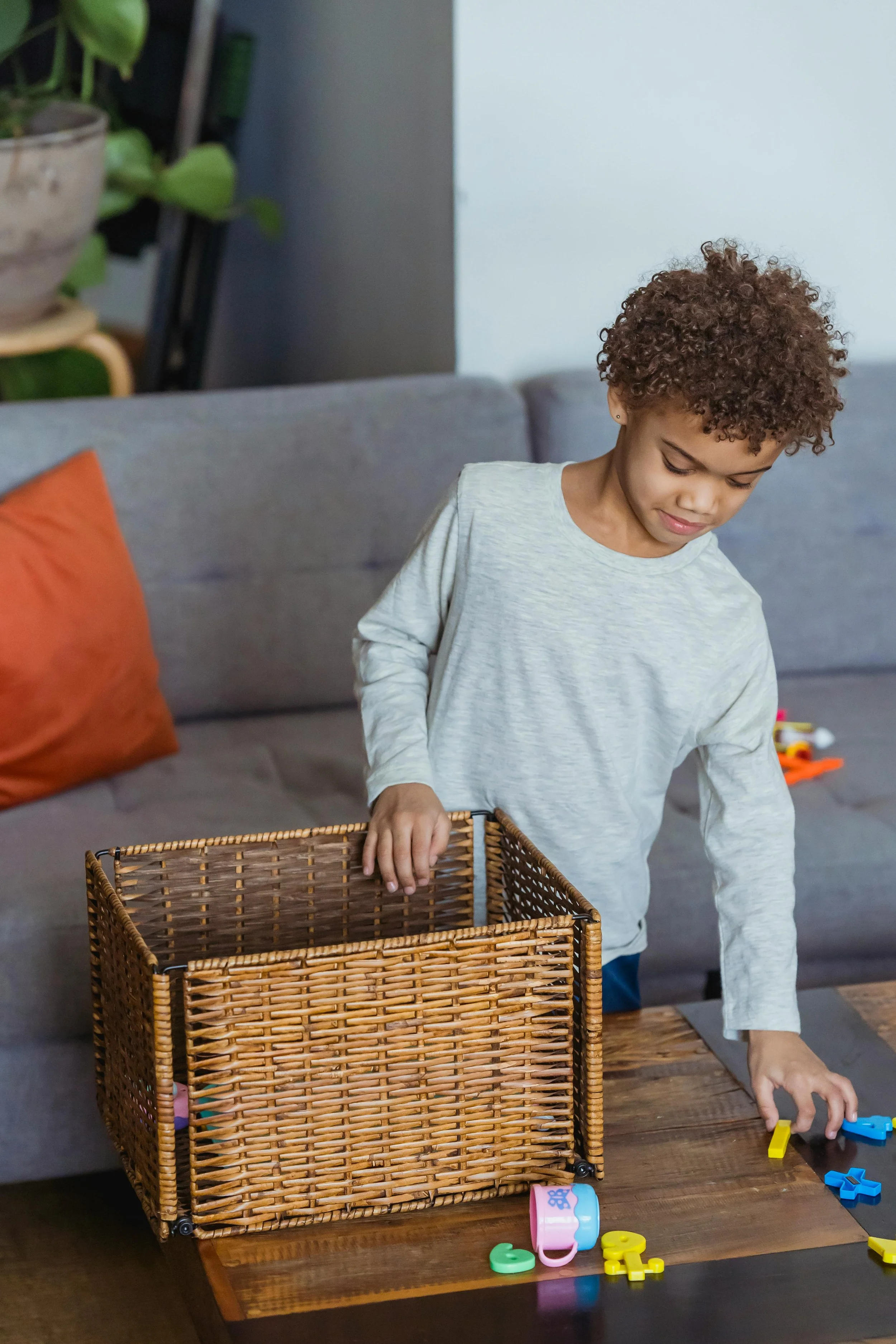 Child putting toys into a woven basket during cleanup time.