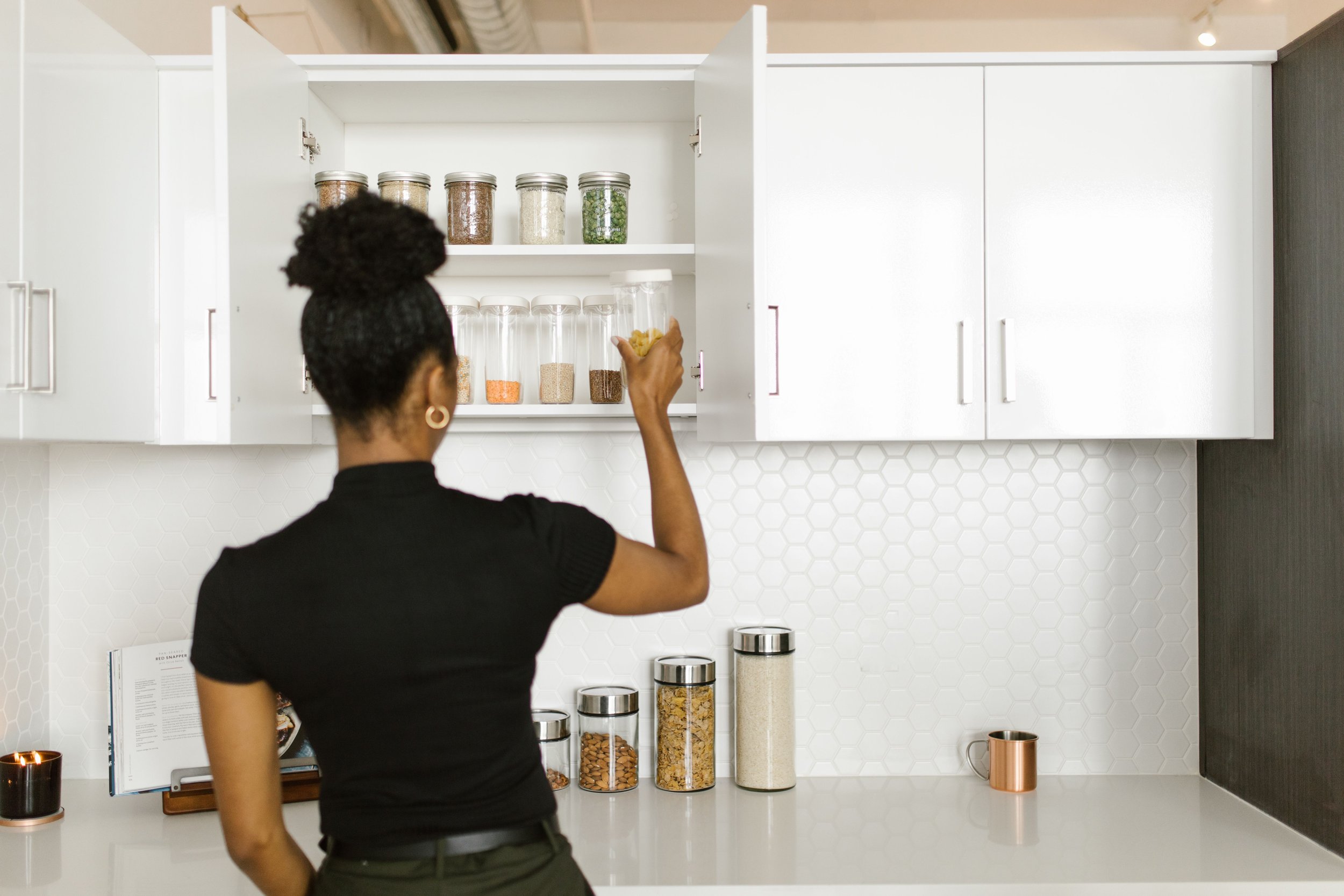 Woman placing a food container in an organized kitchen cabinet with neatly arranged pantry staples.