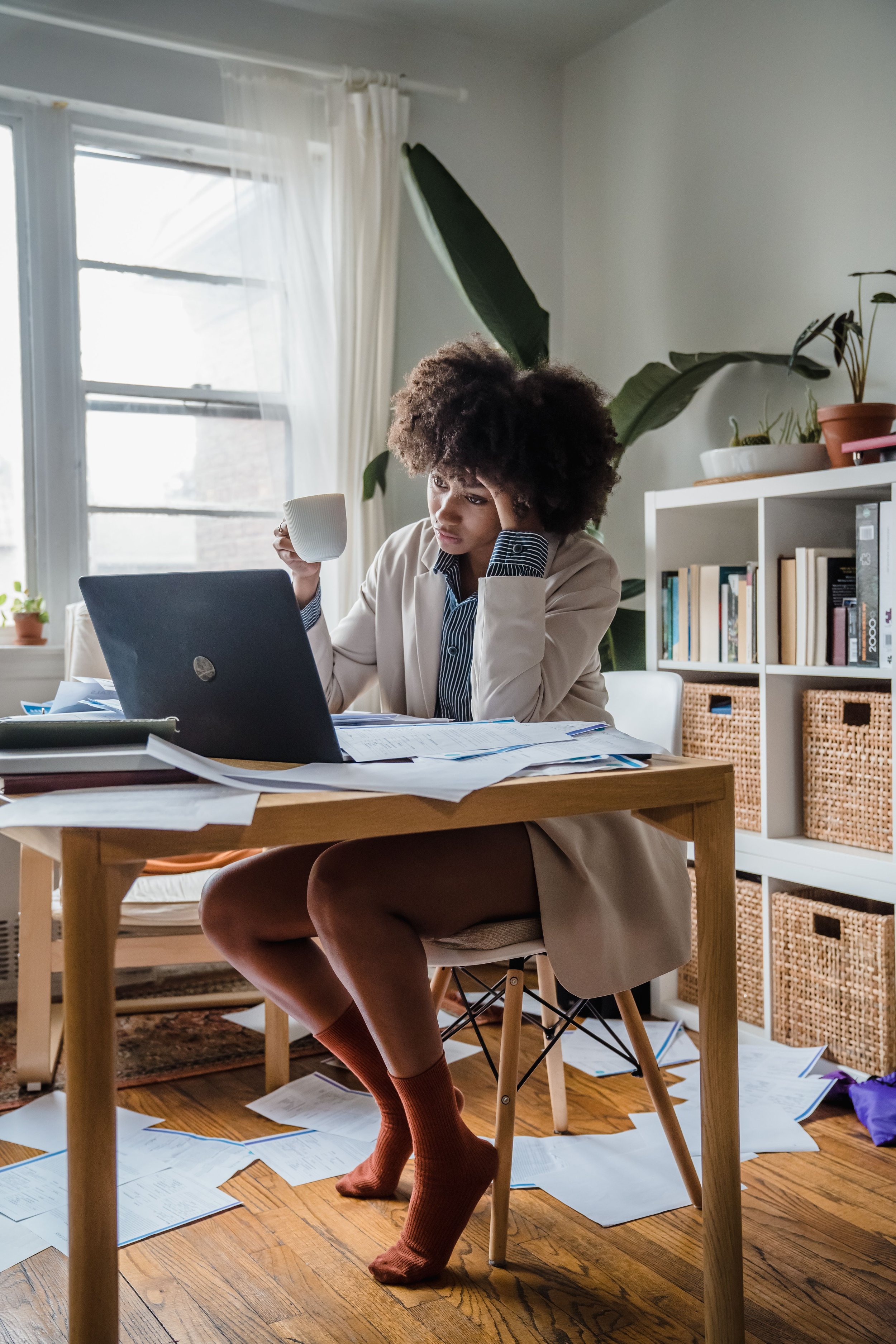 Overwhelmed woman at a cluttered home workspace experiencing situational disorganization.