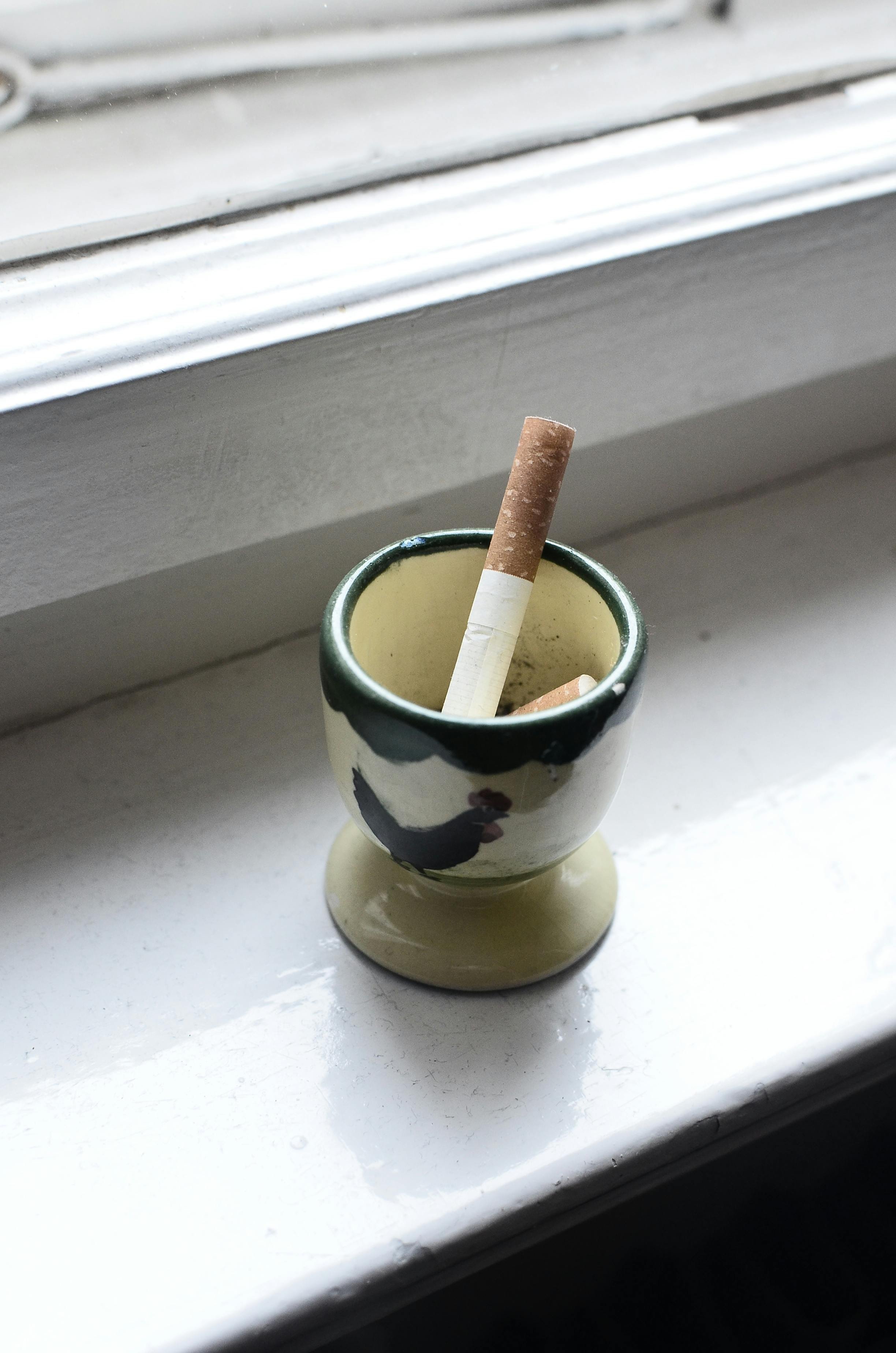 Cigarette in a small ashtray on a windowsill, representing a home where virtual organizing support can gently guide progress despite tobacco odor.