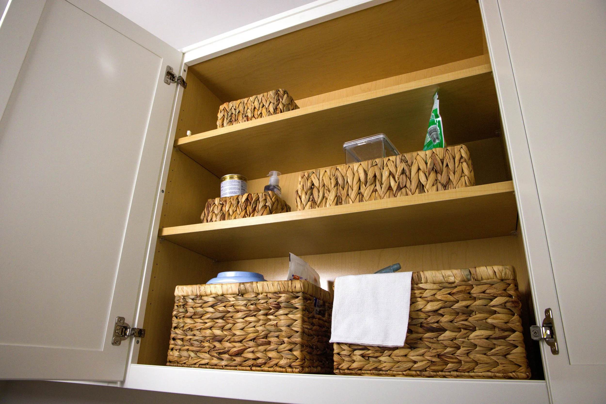 Neatly arranged cabinet with woven baskets, illustrating that organizing starts by simplifying what you already have before adding more.