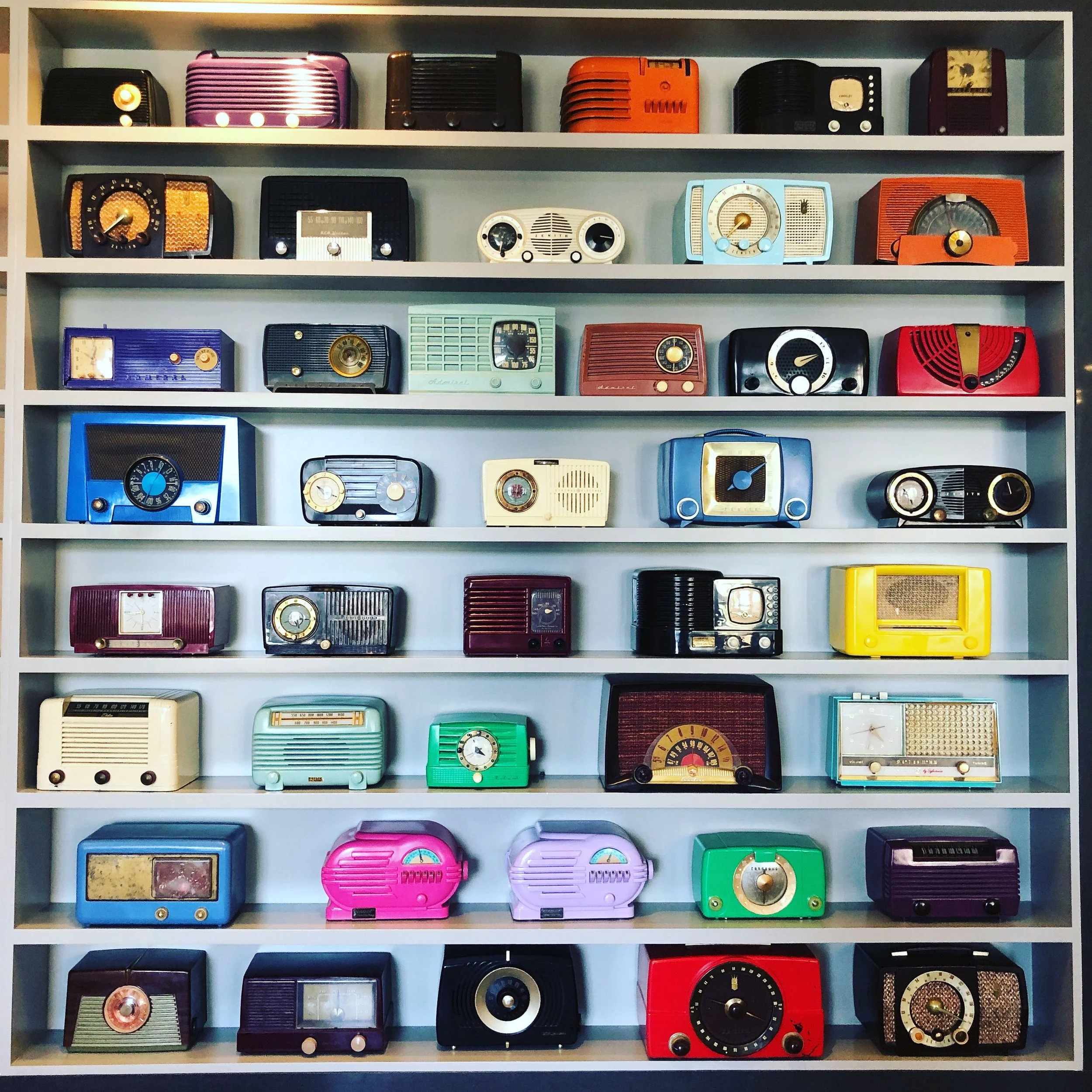 A colorful collection of vintage radios displayed neatly on built-in shelves, illustrating how thoughtful organization creates space to enjoy the things you love without sacrificing beauty, function, or peace.