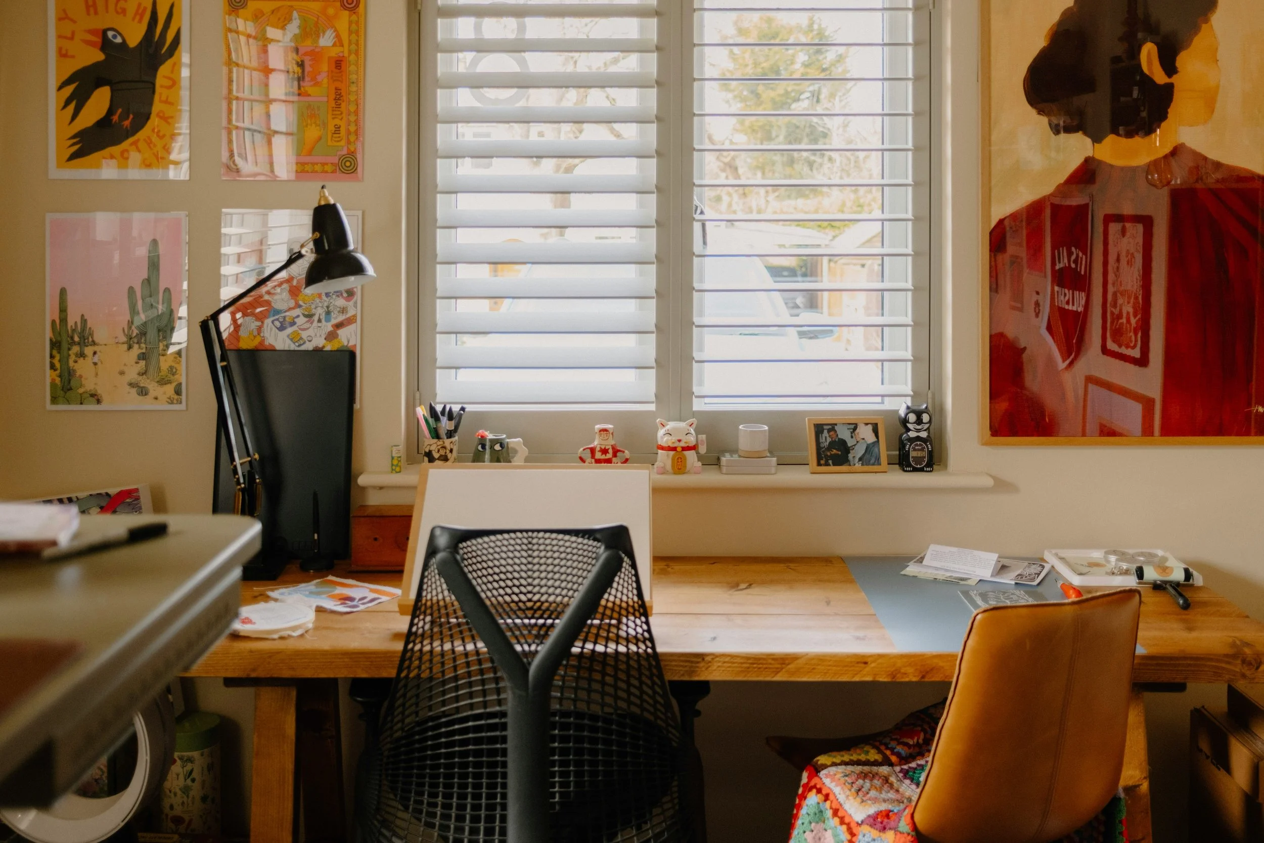 Organized creative workspace with a clear wooden desk, art supplies, and colorful artwork.