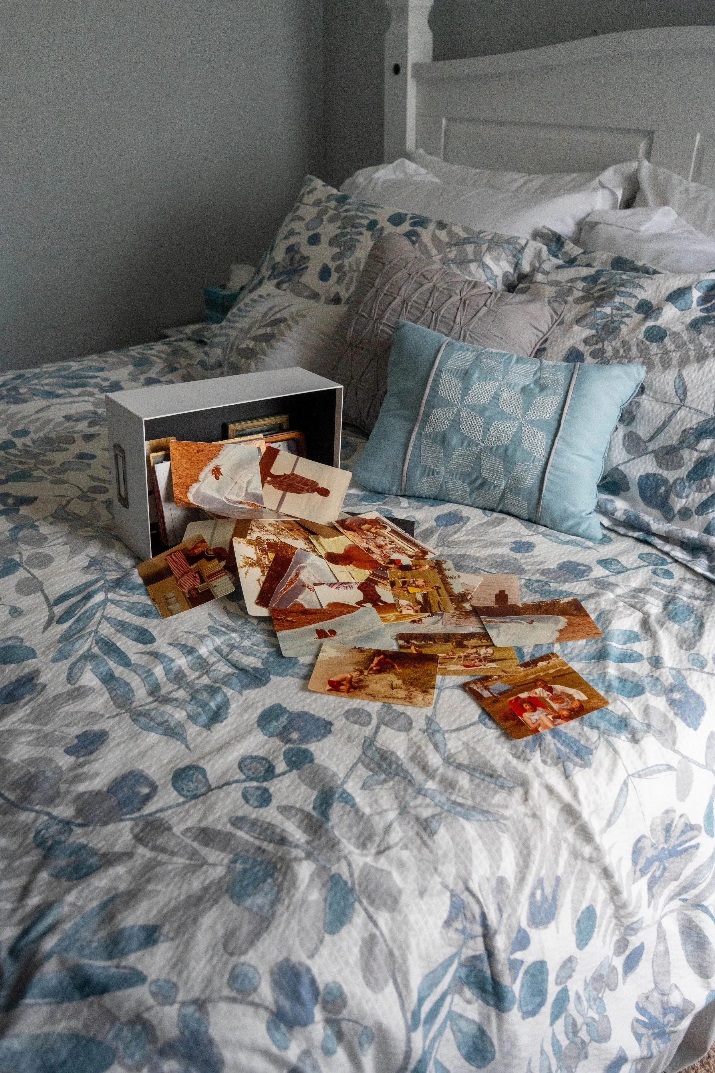 Vintage family photographs spread across a neatly made bed beside a keepsake box, symbolizing preserving treasured memories and the stories we leave behind.