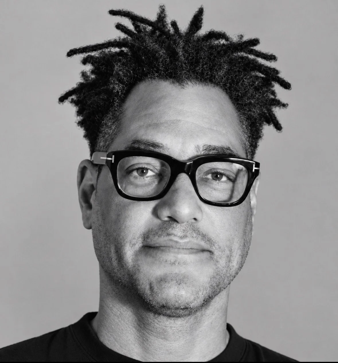 Black and white portrait of a man with short, textured hair, wearing rectangular glasses, looking slightly to the side.