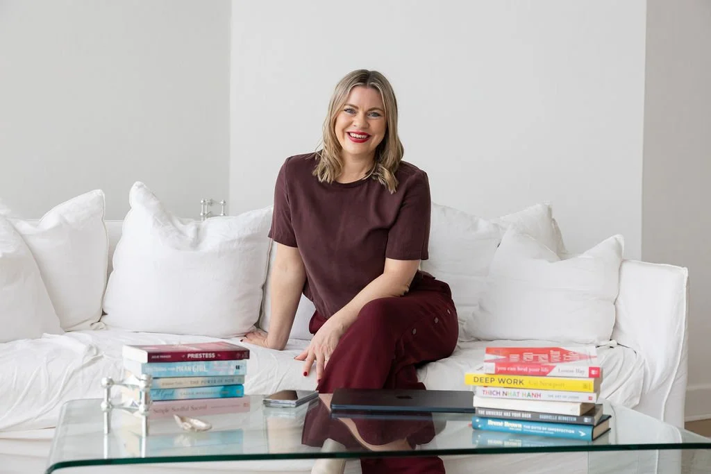 Portrait of Bec Sands, sitting on a lounge with her favourite books