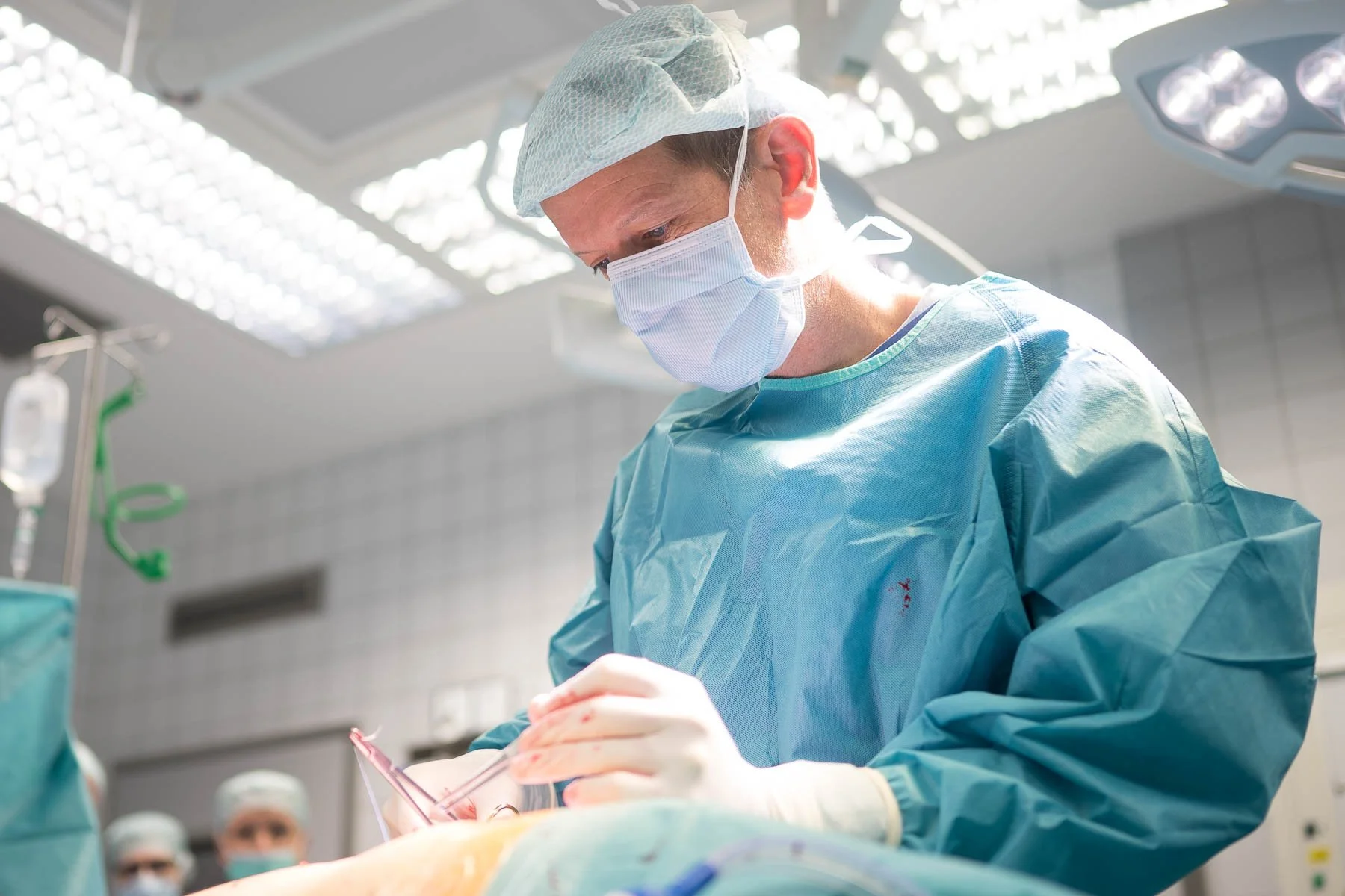 Chirurg bei einer Operation im Operationssaal, trägt Schutzmaske, Kittel und Haube.