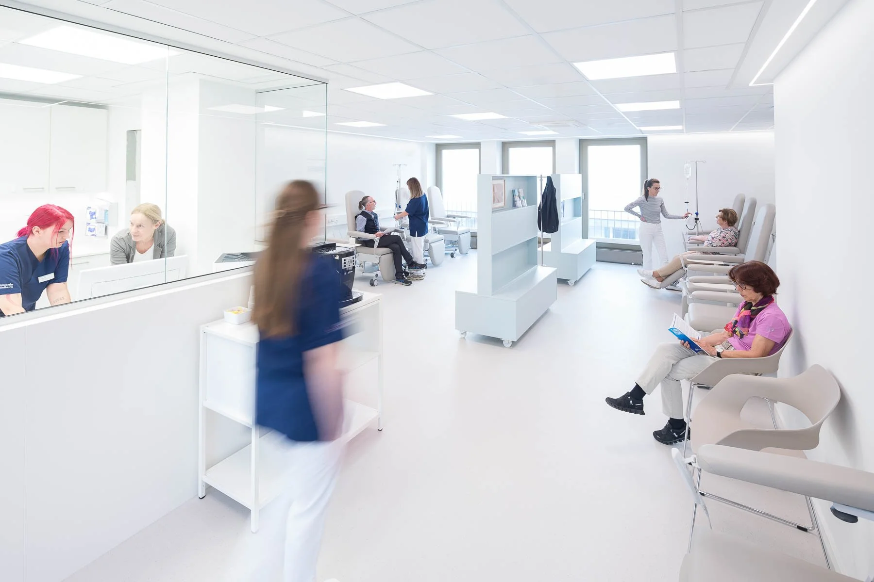 Innenansicht einer modernen Krankenhaushalle mit wartenden Patienten, medizinischem Personal, Ärzten und Pflegekräften, die Behandlungen durchführen und Patienten betreuen.