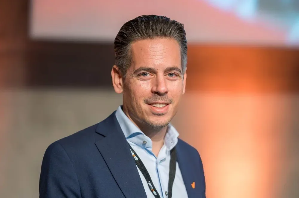 Porträt eines Mannes in formeller Kleidung vor buntem Hintergrund.