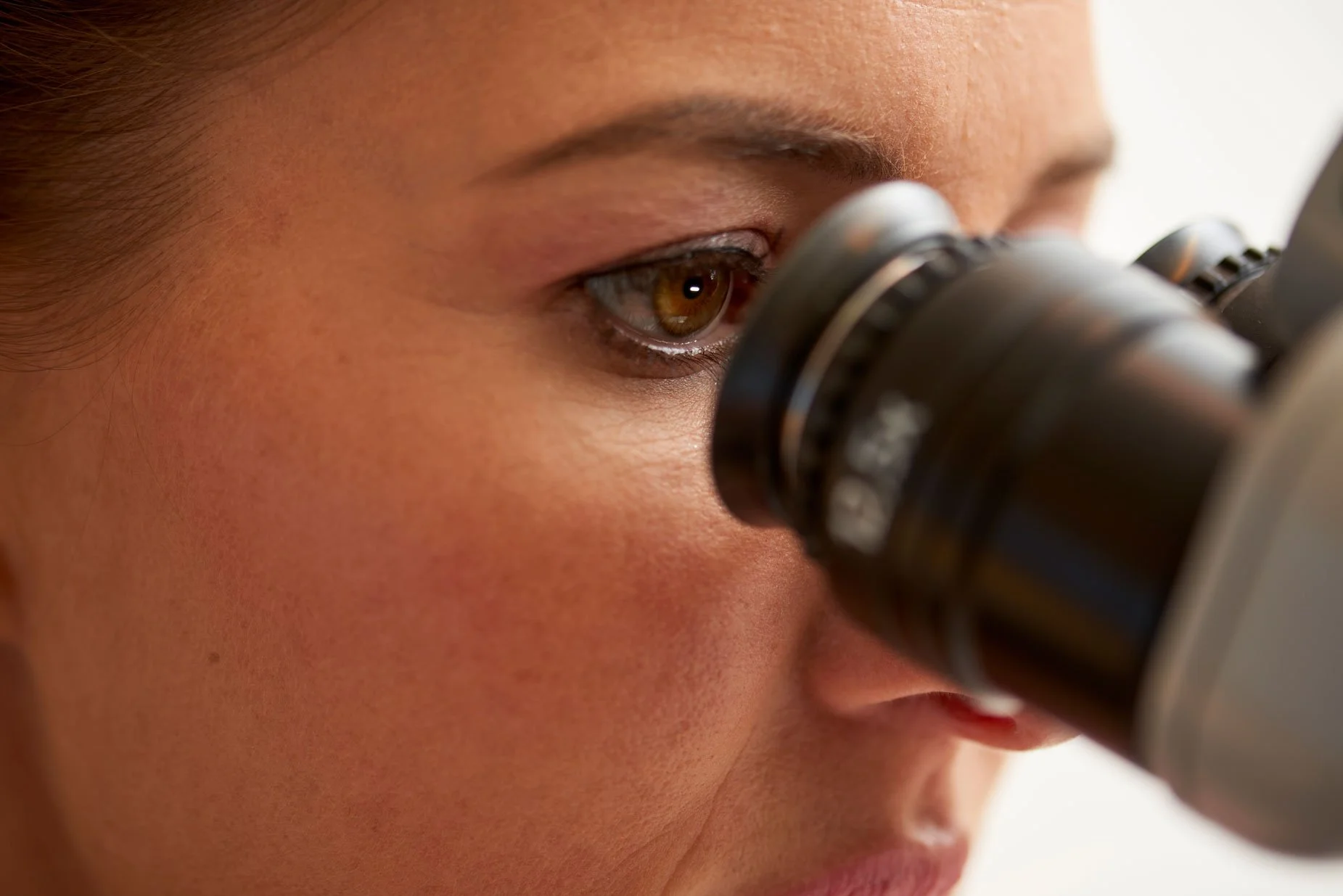 Nahaufnahme eines Menschen, der durch ein Mikroskop schaut.