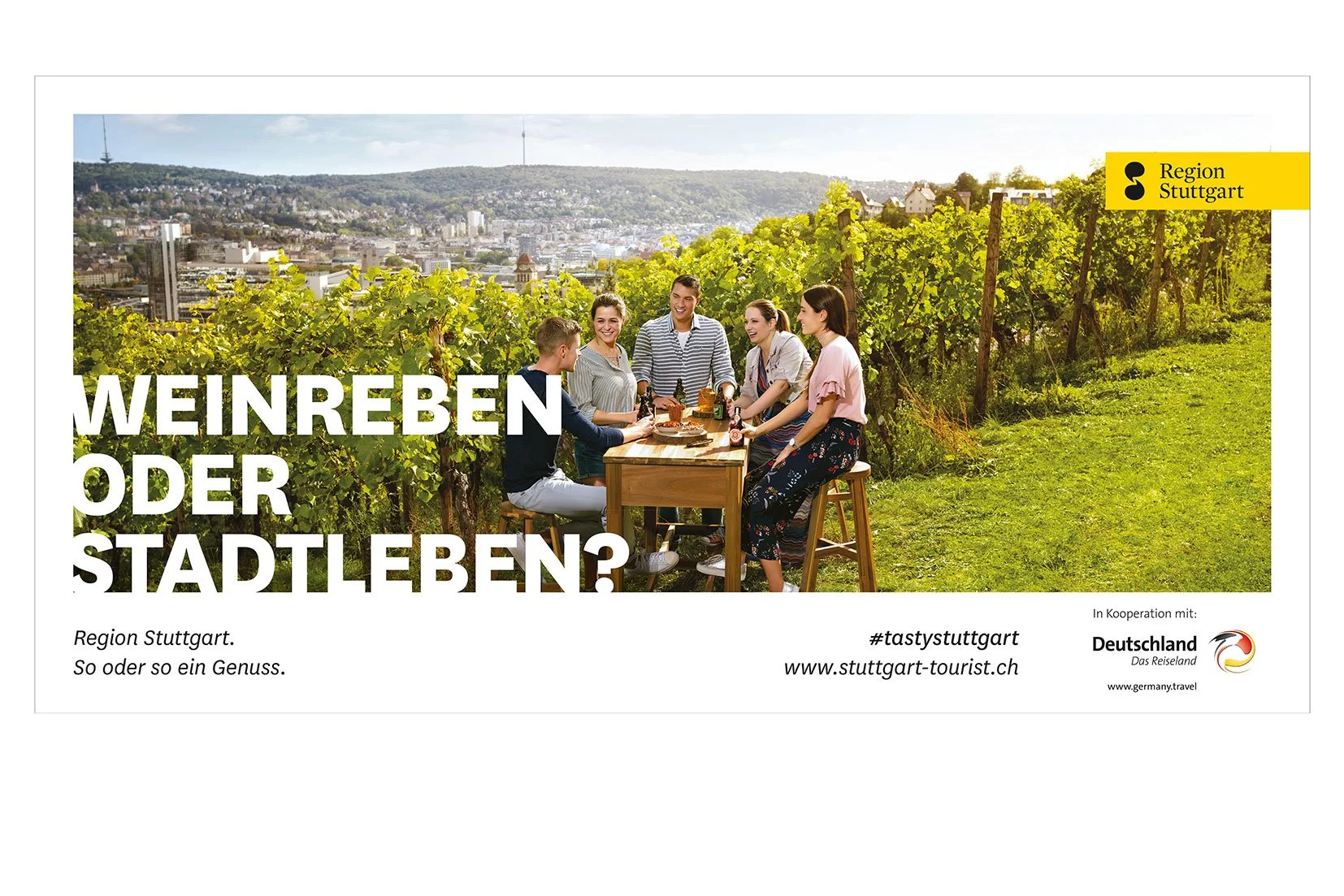 Eine Gruppe von sechs Menschen sitzt an einem Holztisch in einem Weinberg mit Blick auf eine Stadt, sie unterhalten sich und genießen Essen und Getränke bei Sonnenlicht.