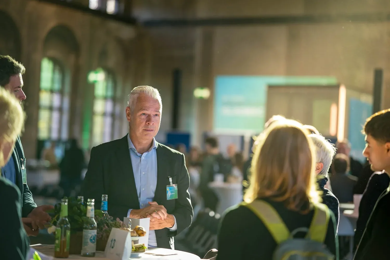 Mann in Anzug bei einer Konferenz im Gespräch mit mehreren Personen in einem großen Raum