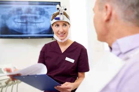 Zahnarzt spricht mit einem Patienten im Behandlungszimmer, während sie eine Unterlage hält.