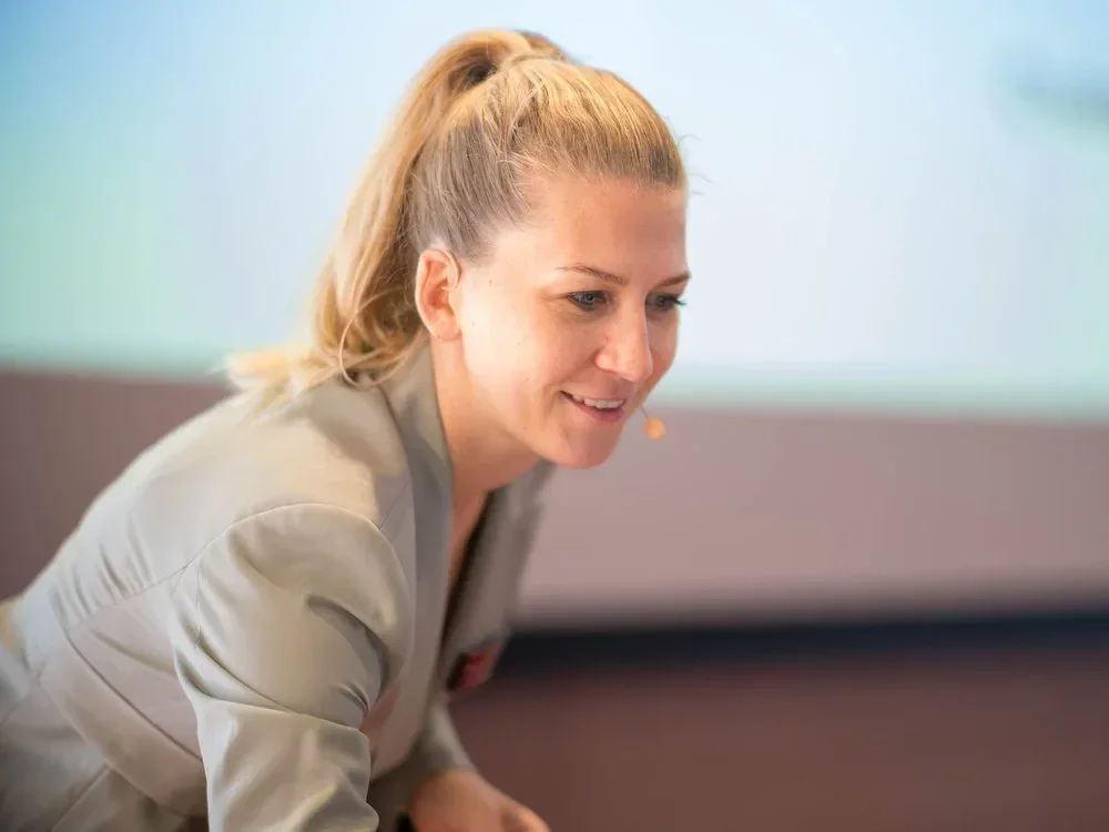 Eine Frau mit einem Mikrofon am Ohr, die lächelnd nach unten schaut.