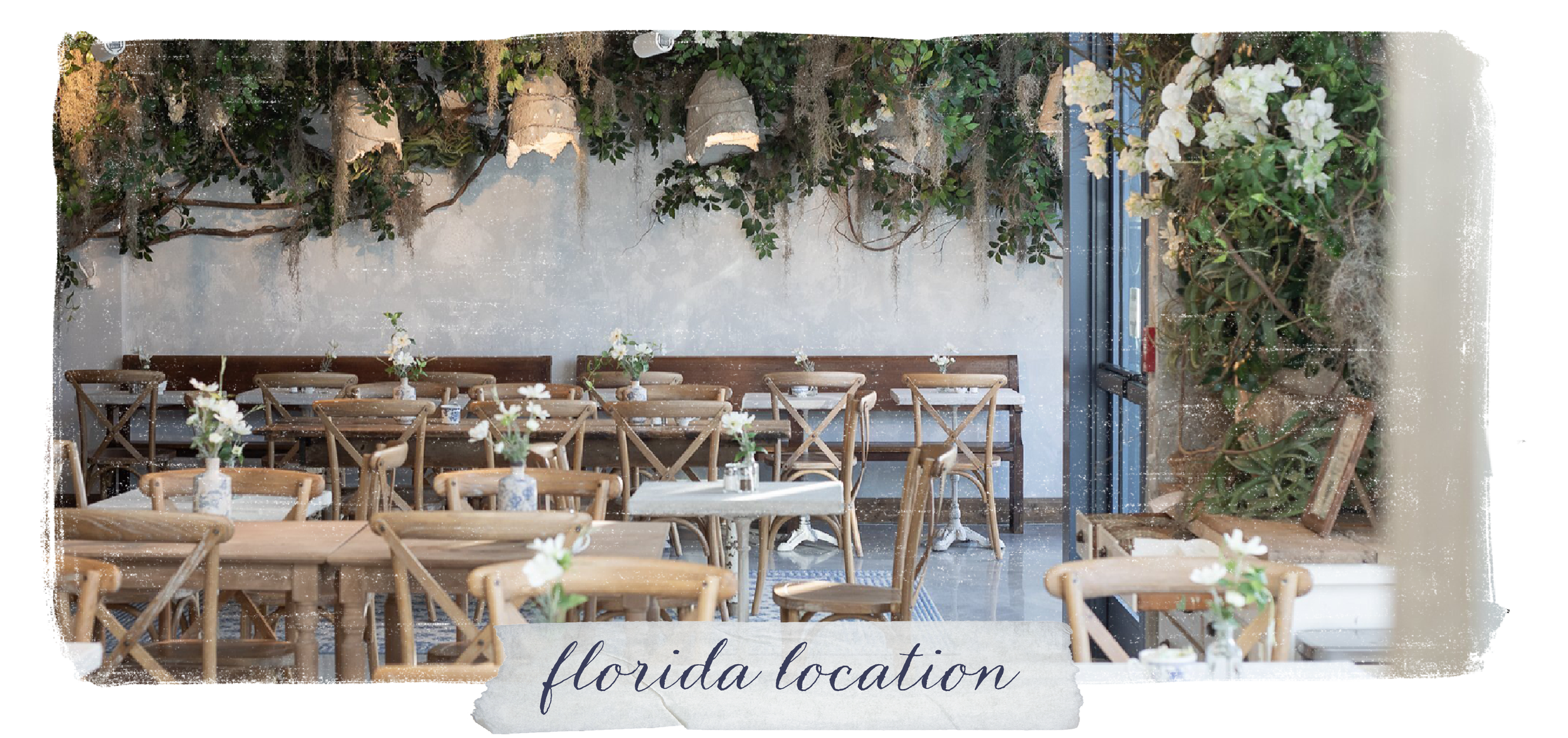 Interior of a restaurant or cafe with wooden chairs and tables decorated with small floral centerpieces. There are hanging planters and greenery on the wall, creating a lush, natural aesthetic.