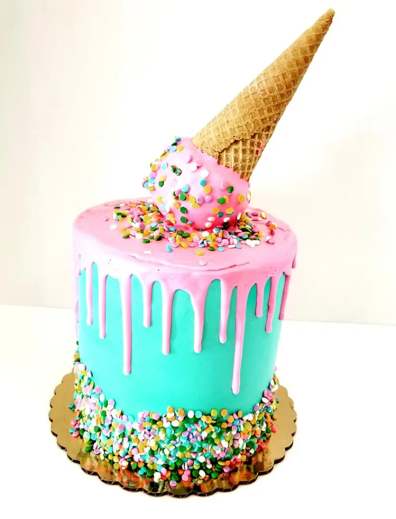 A colorful birthday cake with blue and pink icing, rainbow sprinkles, an ice cream cone on top, and a scoop of ice cream with sprinkles.