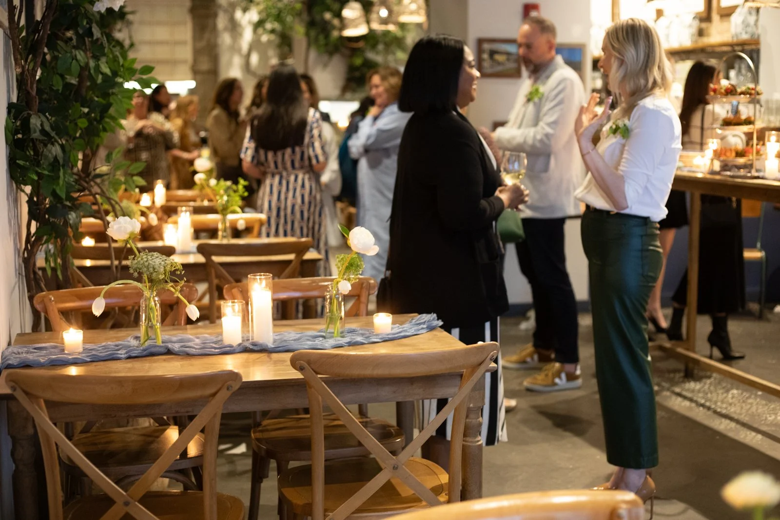 People socializing at a decorated indoor event venue with candles and flowers.
