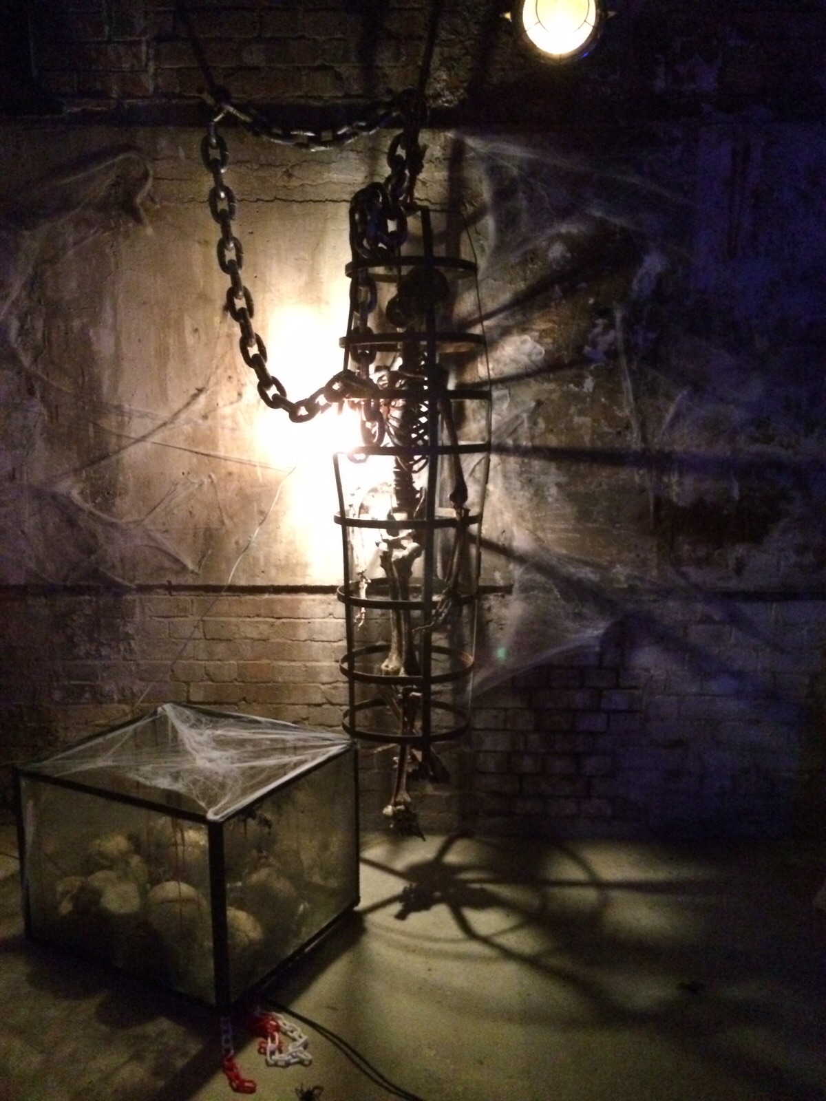 skeleton in rusted cage with yellow light behind.