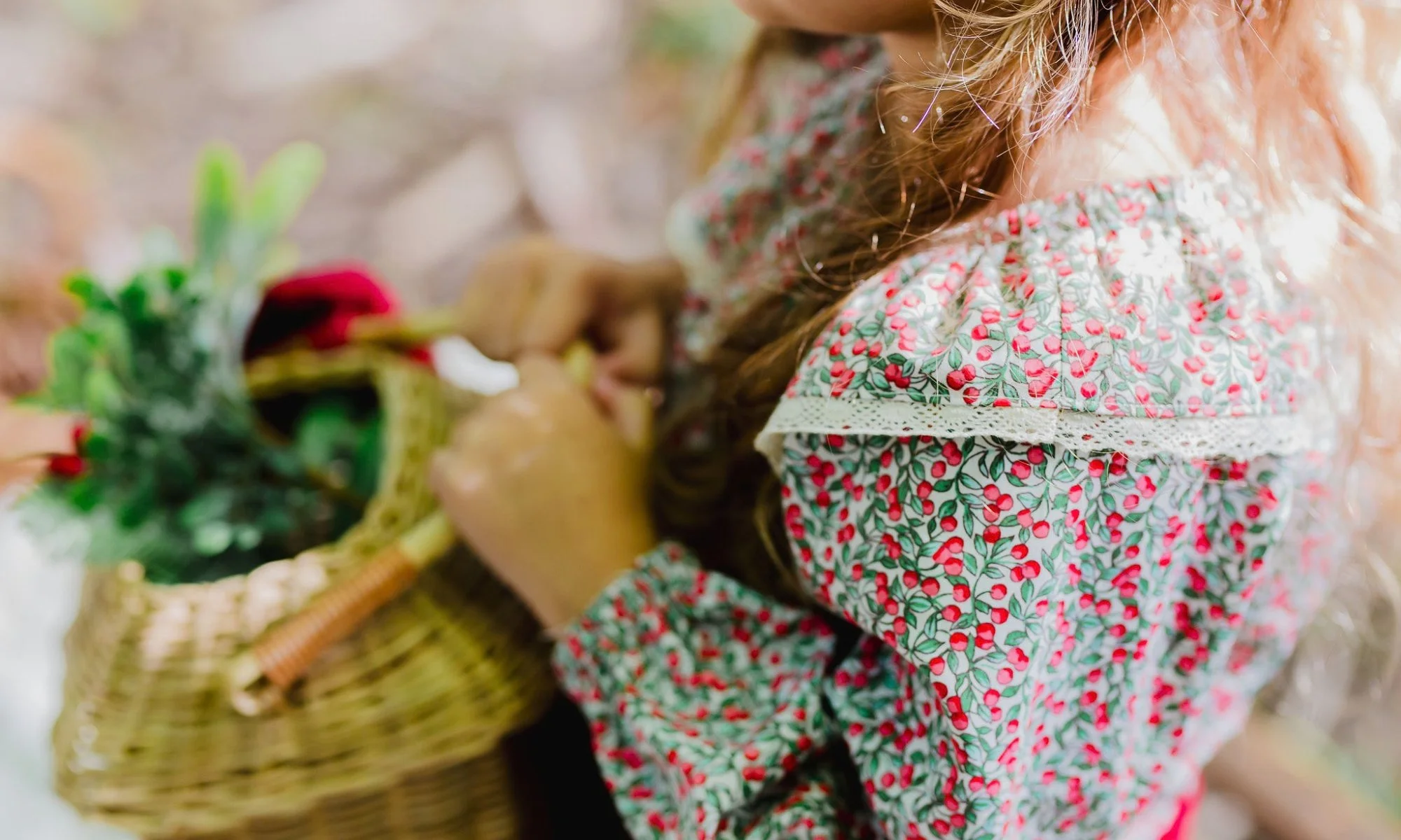 Close-up of a girl in a floral dress carrying a woven basket filled with plants and flowers.