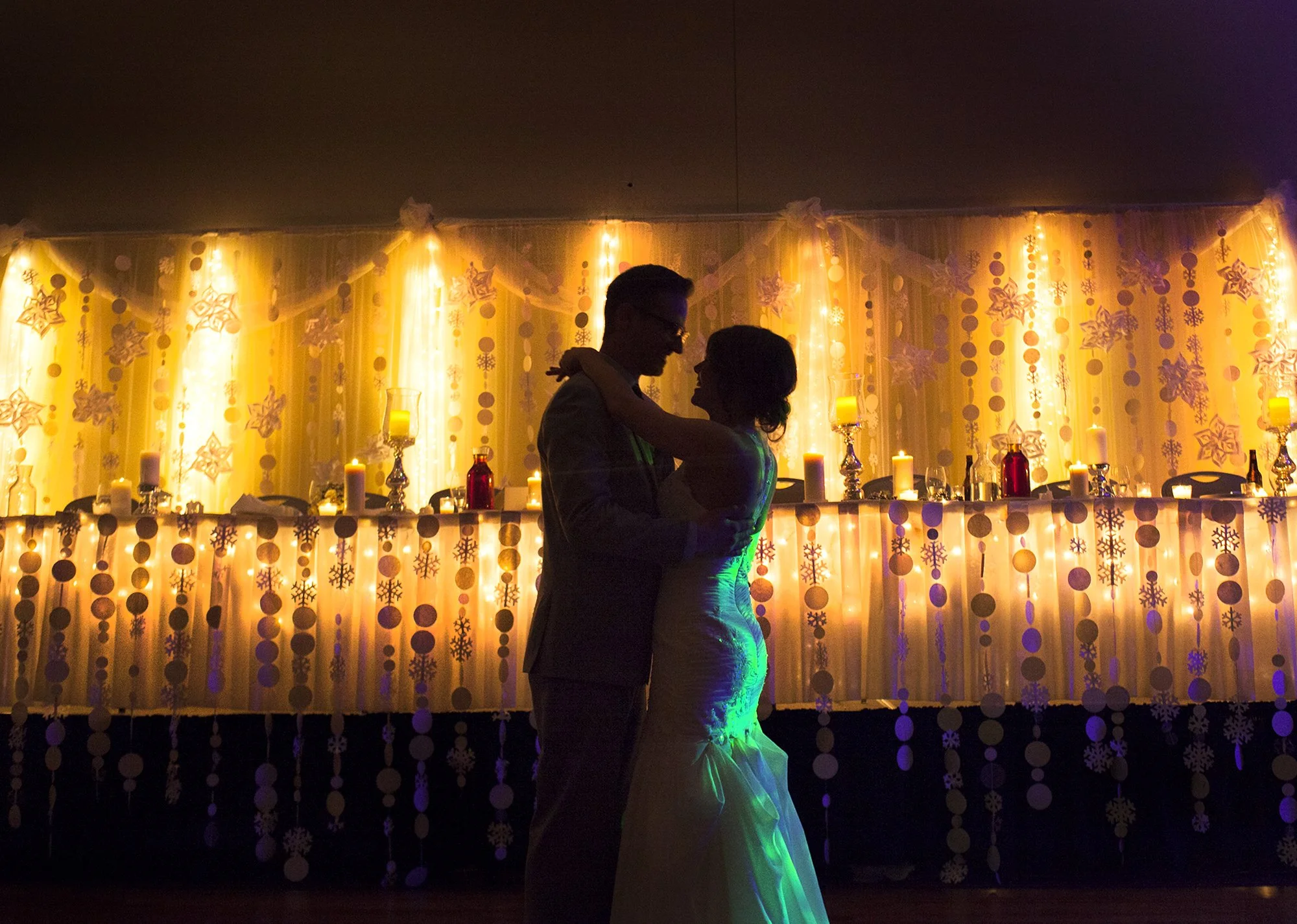Bride and groom sharing their first dance in front of warm golden wedding lights and winter-themed decorations.