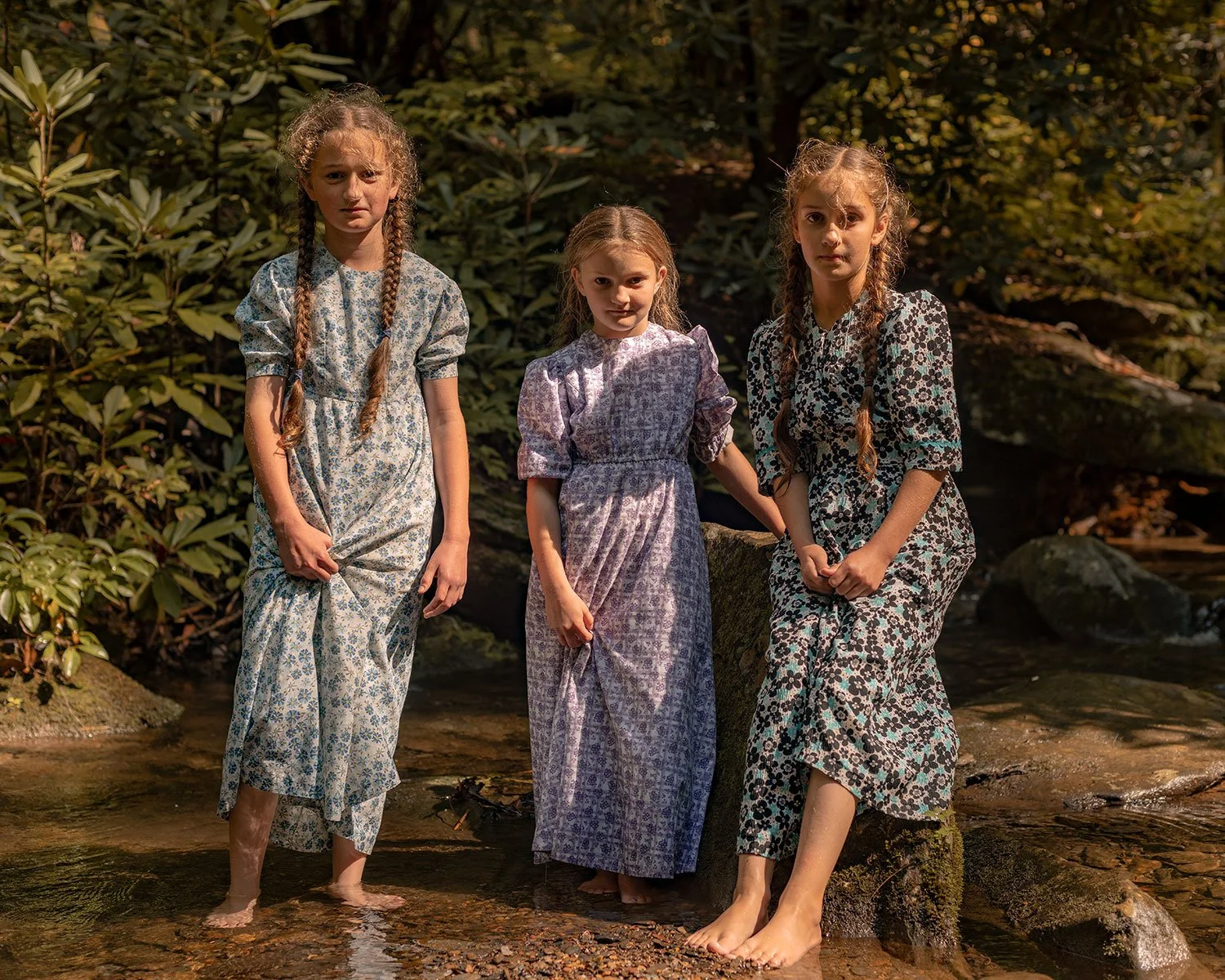 Three young Mennonite girls stand in a running stream in long dresses near the Smoky Mountain National Park in East Tennessee