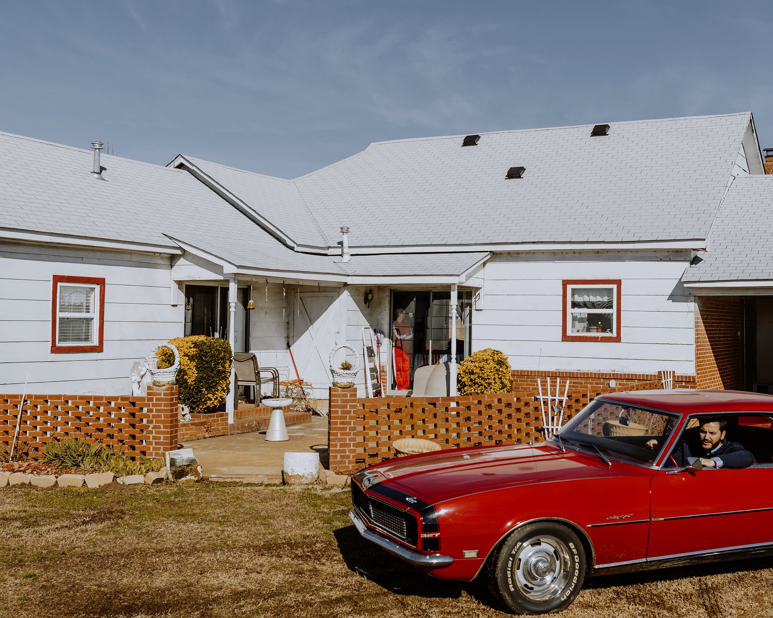 A vintage red car parked in front of a rural farm house in western Arkansas