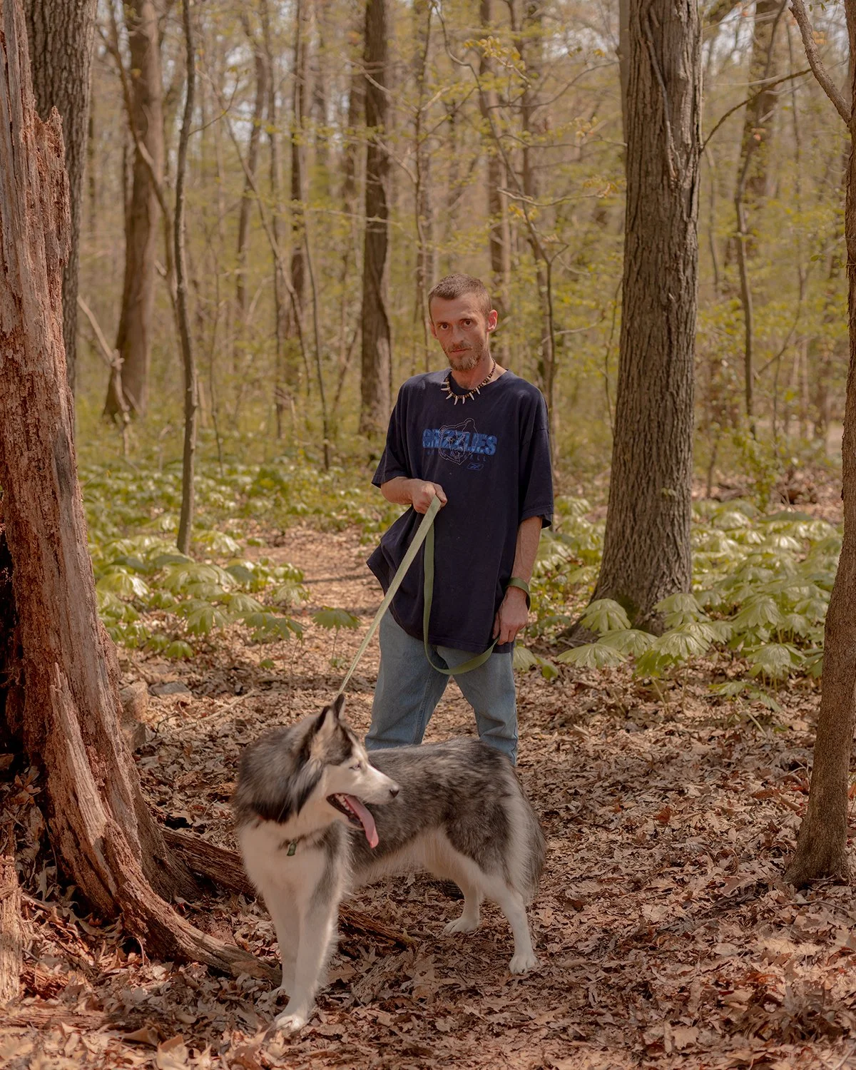 A man walks a wooded path with his husky dog at Overton Park in Memphis, Tennessee