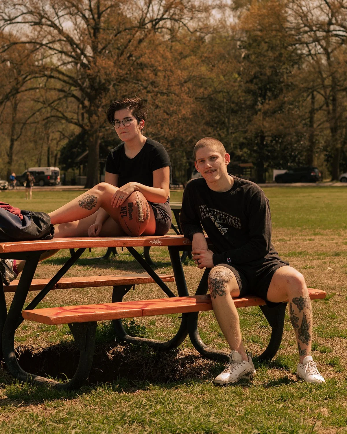 A young couple with tattoos sit on a picnic table with a football at Overton Park in Memphis, Tennessee