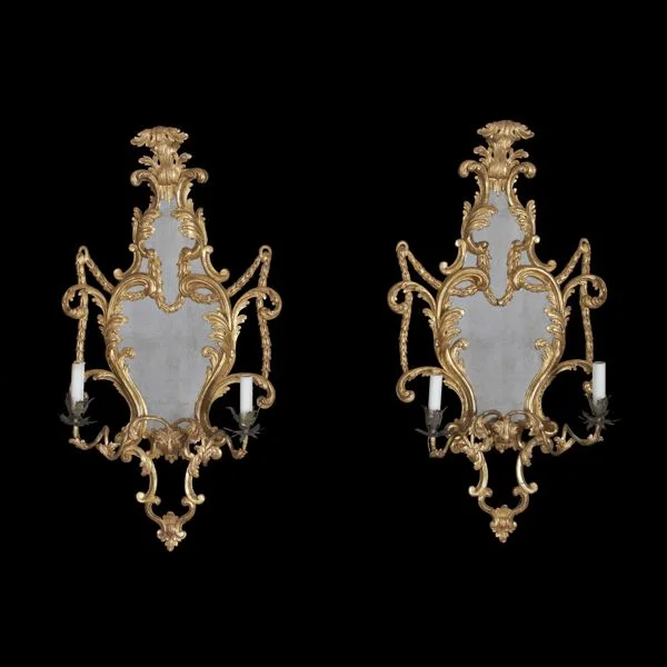 A fine pair of Rococo carved gilt wood cartouche form Girandole two – arm sconce mirrors. Having carved acanthus and bellflowers. England, 18th Century.