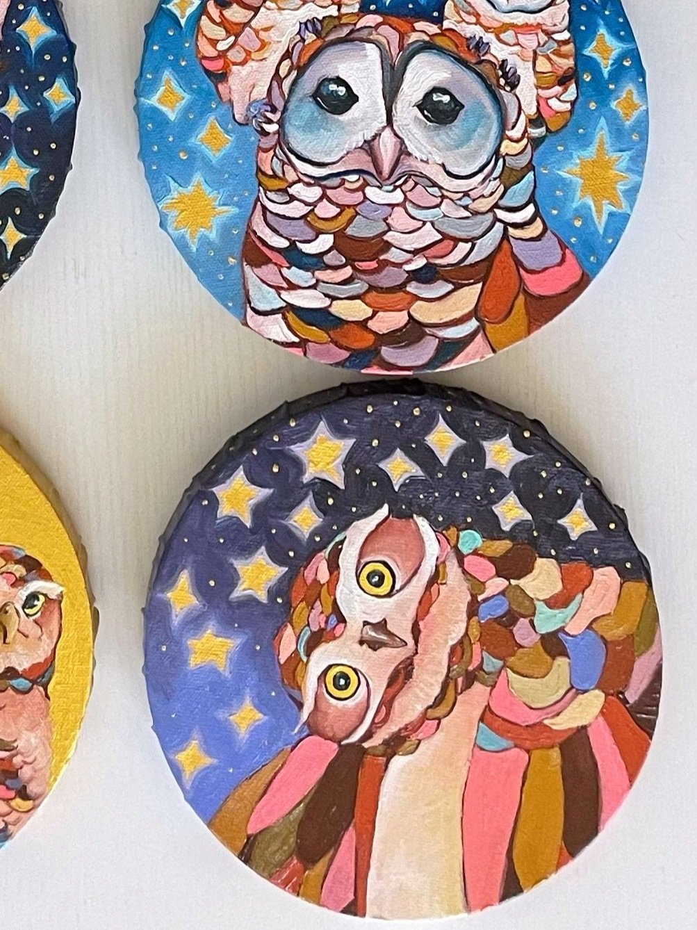 nine round paintings of owls arranged on a white table