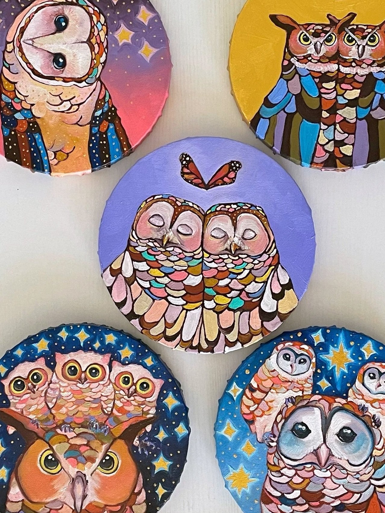 nine round paintings of owls arranged on a white table