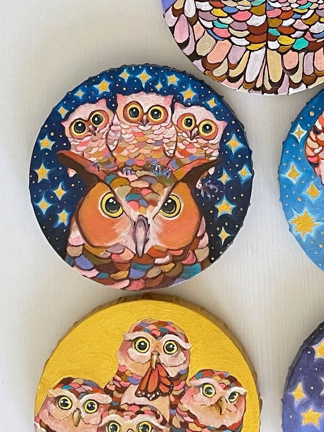 nine round paintings of owls arranged on a white table