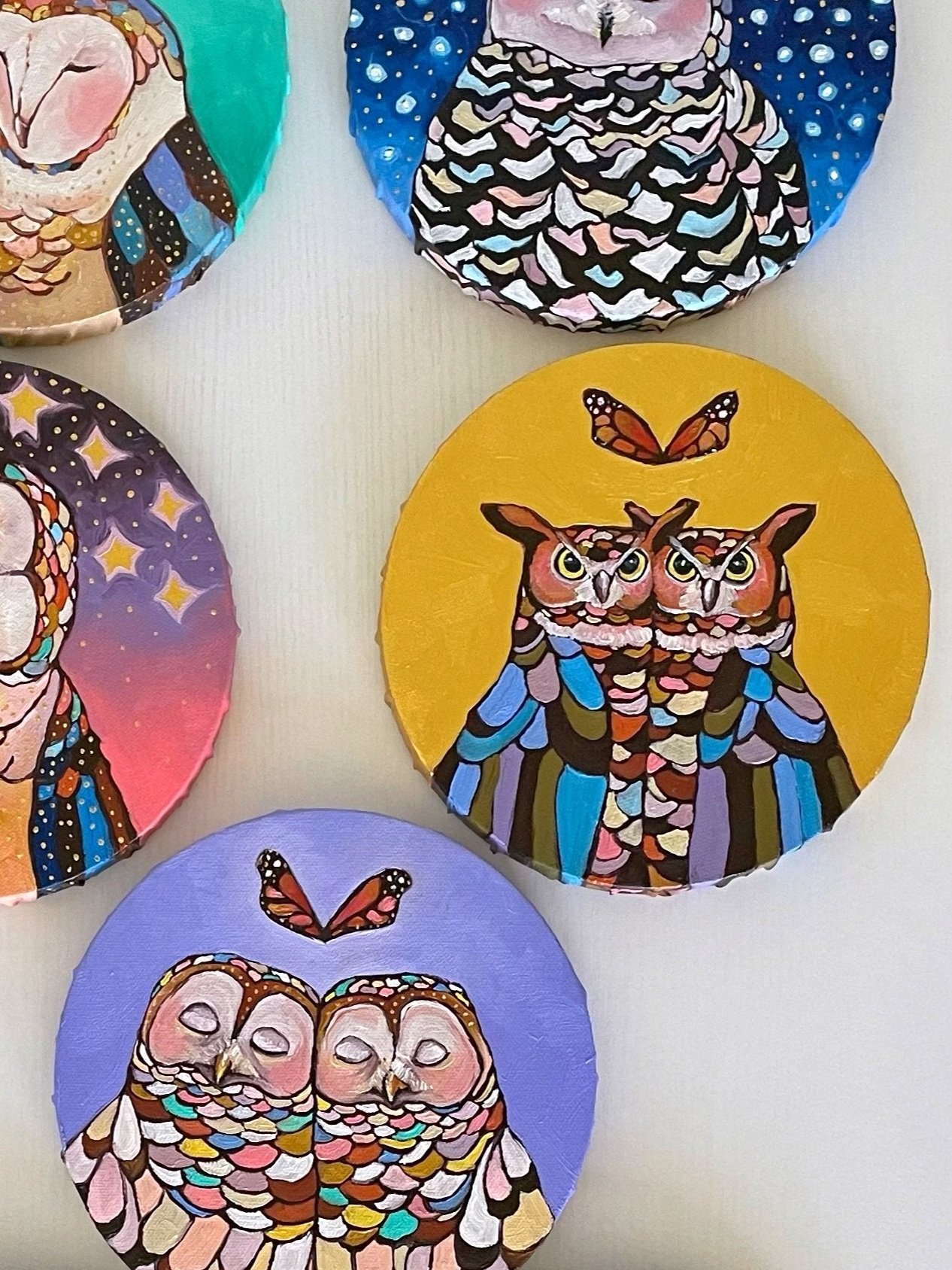 nine round paintings of owls arranged on a white table