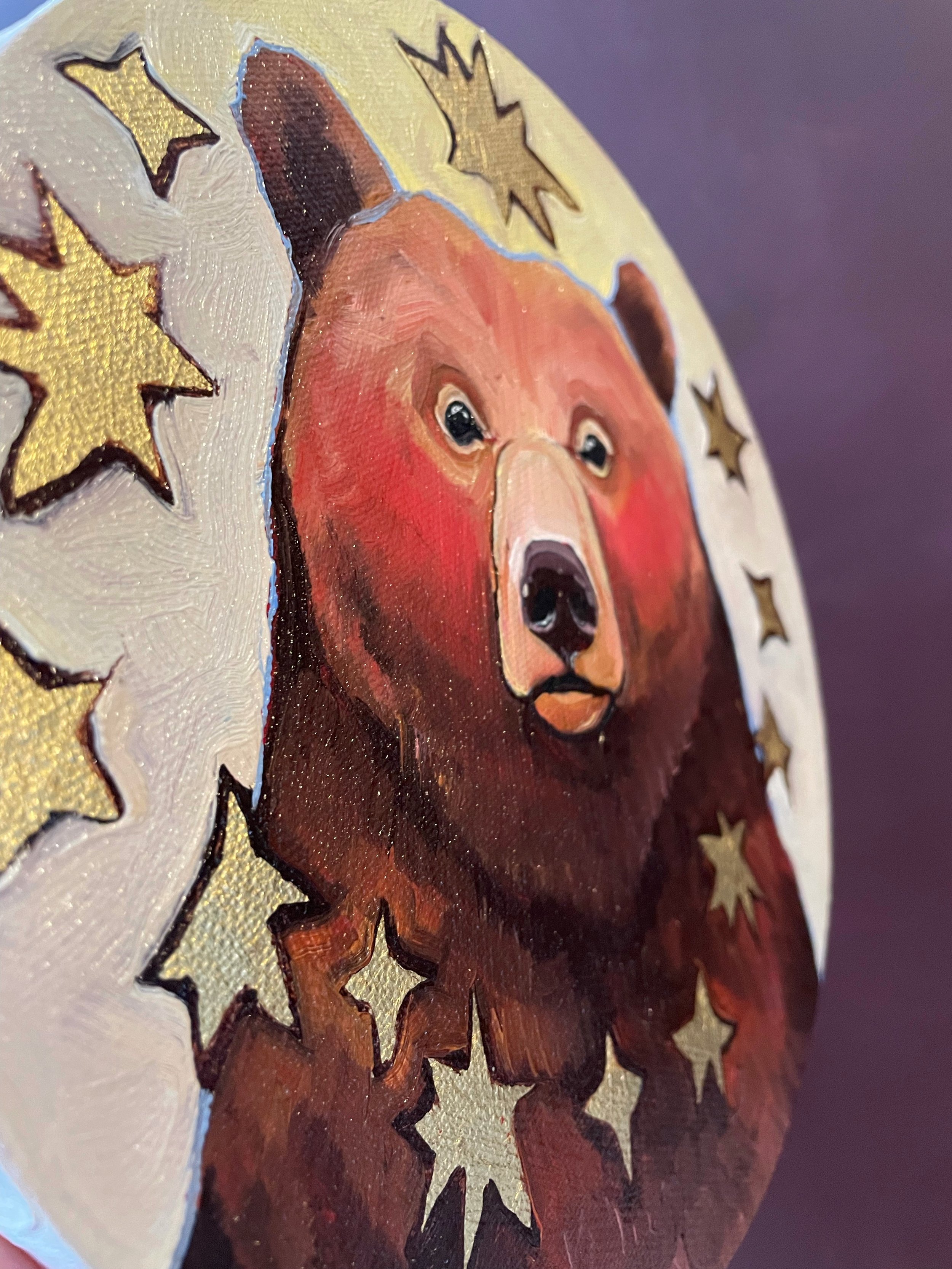a side view on a round painting of a brown bear surrounded by golden stars