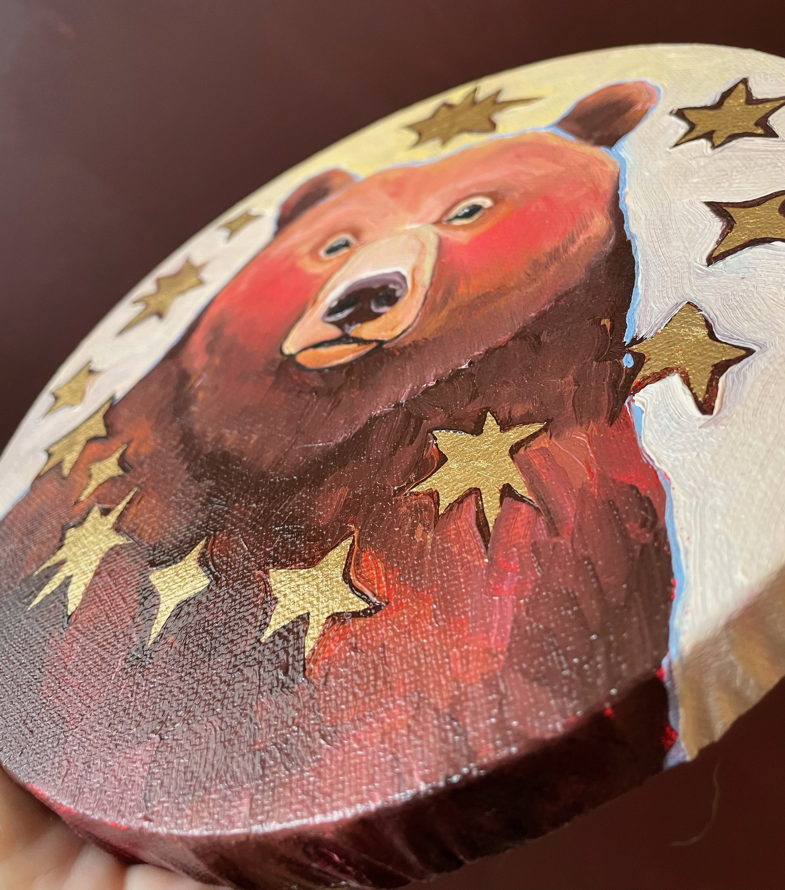 another angle on a round painting of a brown bear surrounded by golden stars